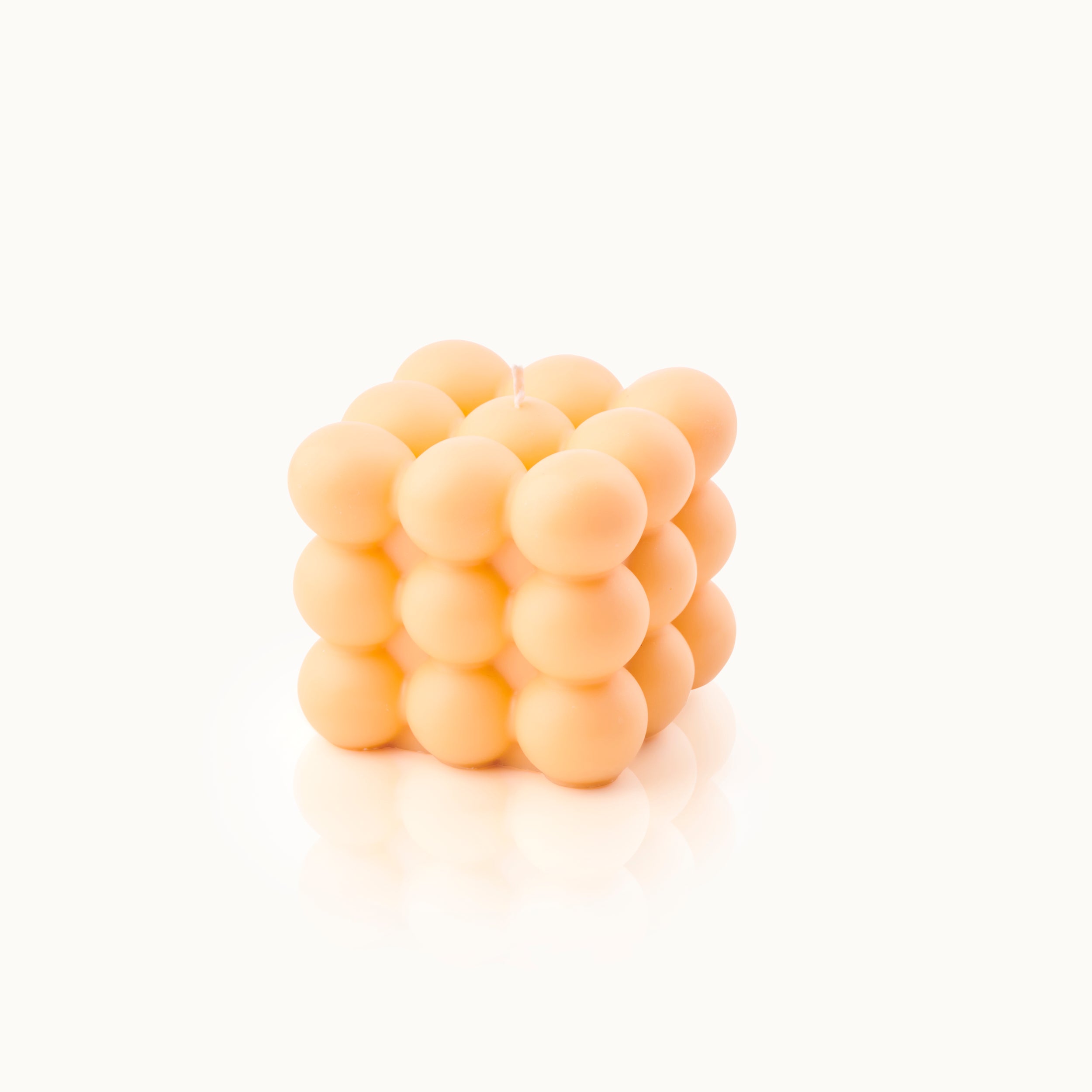 Orangefarbene Kerze in Würfelform, bestehend aus kugelförmigen Elementen, auf weißem Hintergrund.