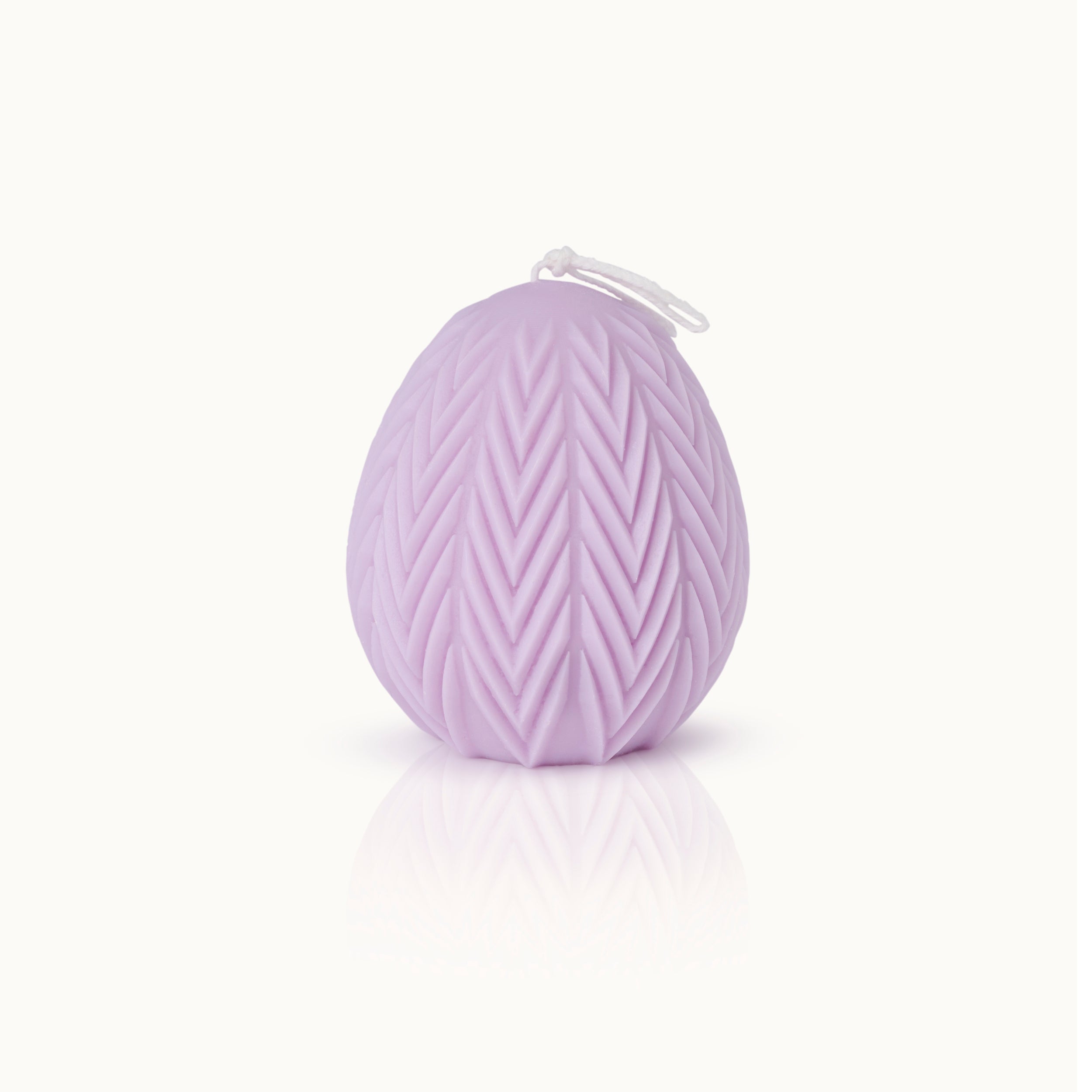 Eine lavendelfarbene, eiförmige Kerze mit einem strukturierten Zickzack-Muster und einem weißen Docht auf der Oberseite, vor einem schlichten weißen Hintergrund.