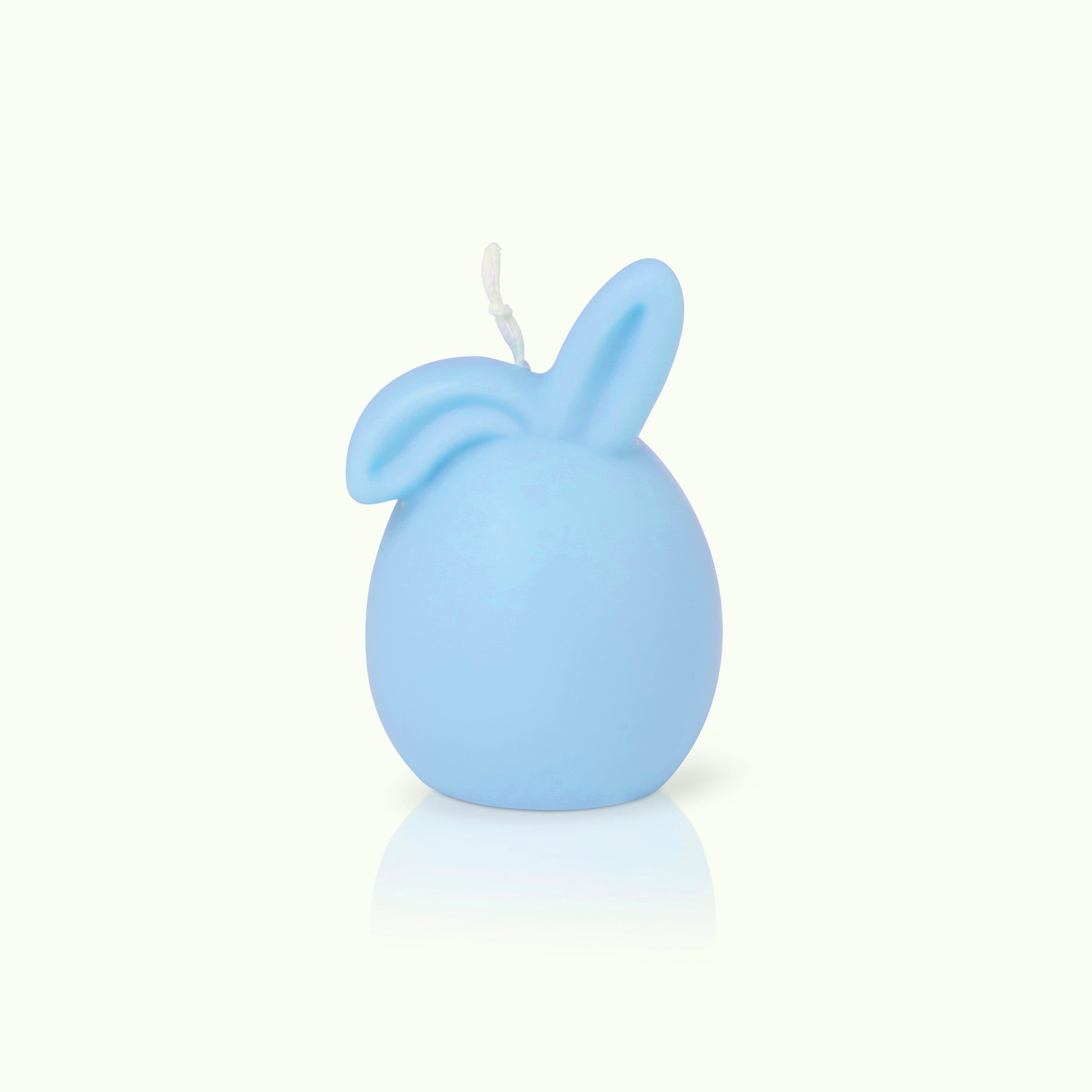 Eine hellblaue Kerze in Form eines Eies mit zwei Hasenohren auf der Spitze, vor einem schlichten weißen Hintergrund.