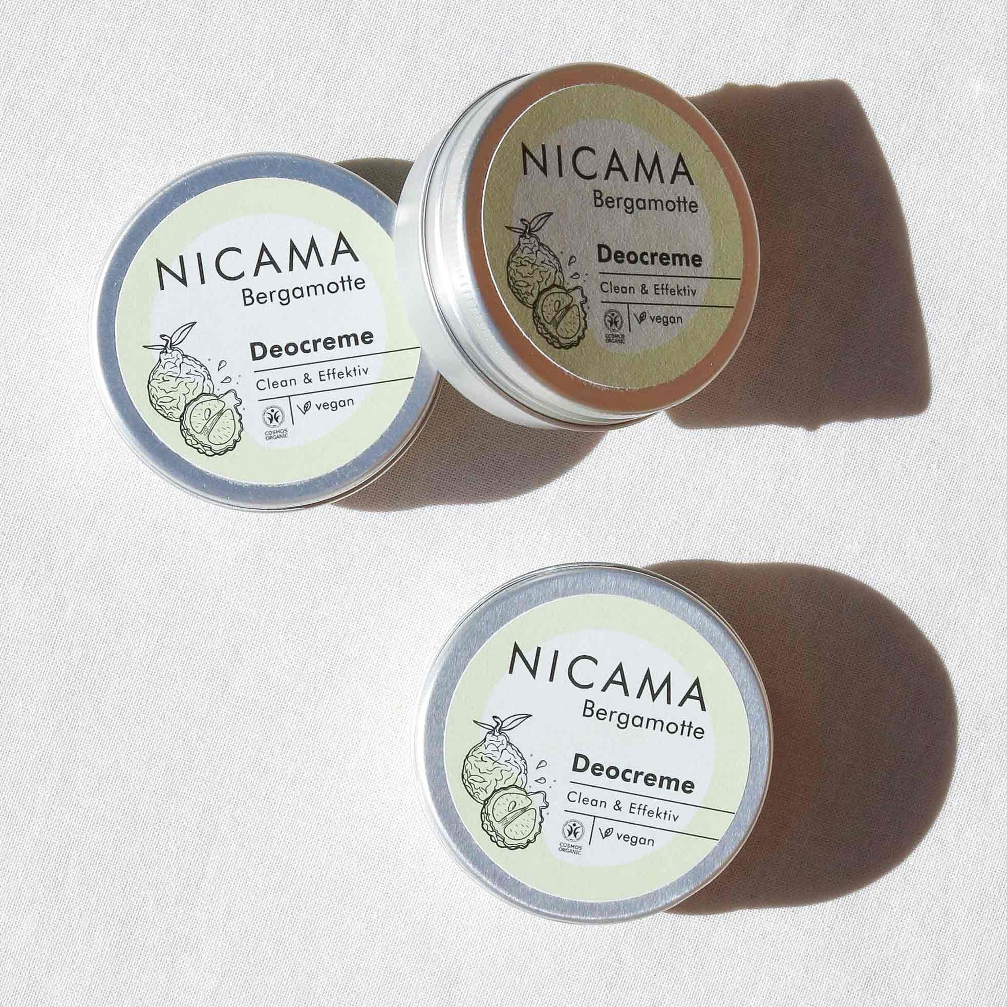 Drei Dosen Nicama Bergamotte Deocreme mit veganem Label auf weißem Hintergrund.