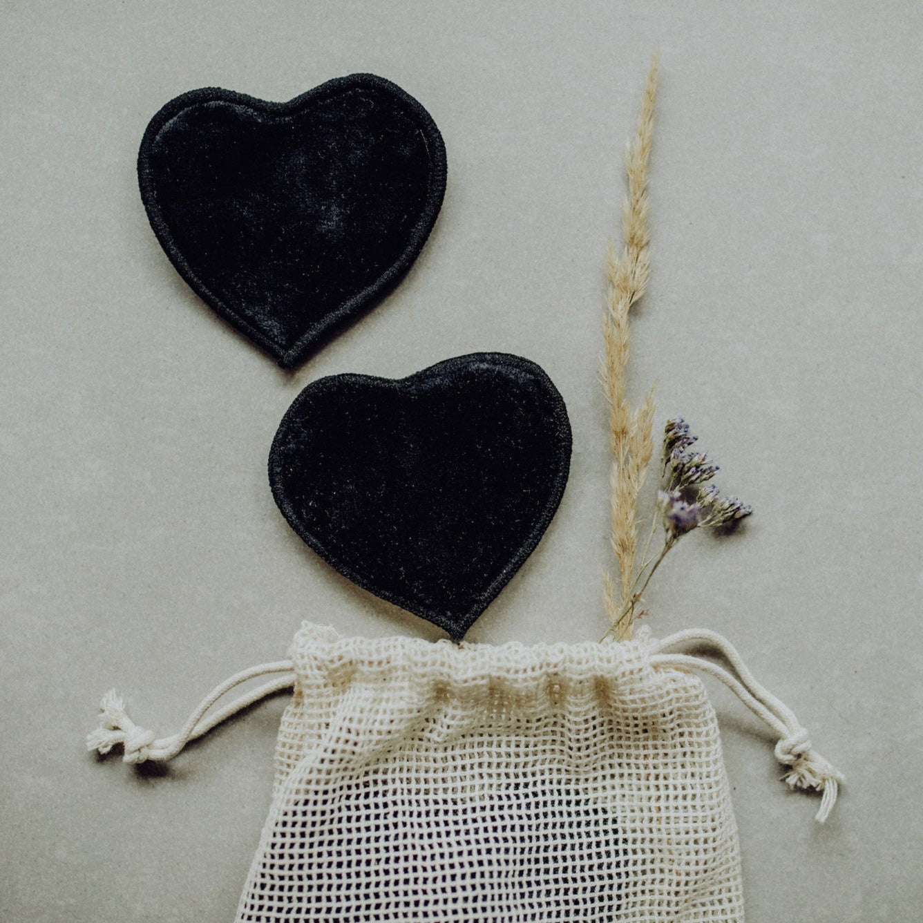 Zwei schwarze Herz-Pads liegen auf einem Tisch neben einem Beutel aus Baumwolle und getrockneten Blumen.