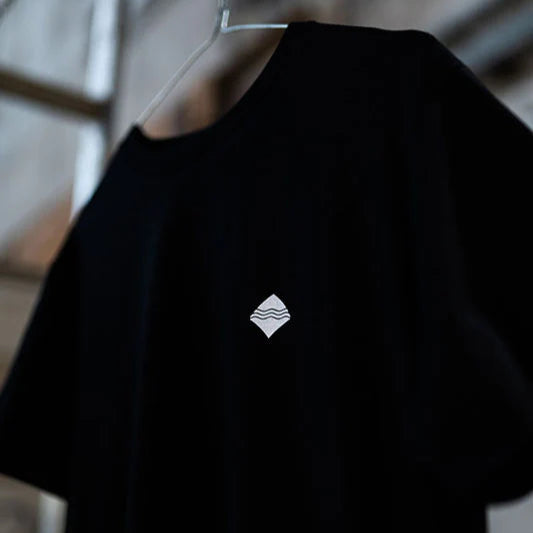 Schwarzes T-Shirt mit kleinem weißen Logo auf einem Kleiderbügel.