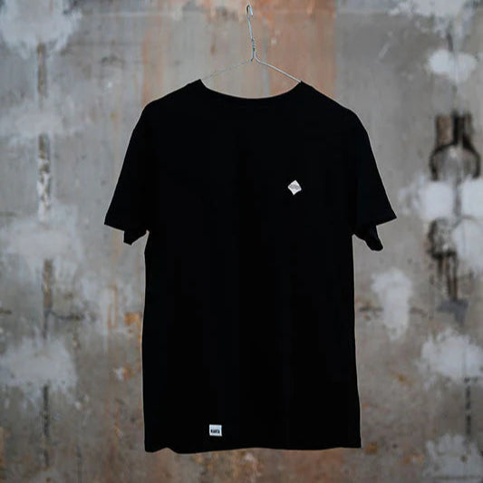 Schwarzes T-Shirt mit kleinem Logo auf der linken Brust, hängt an einem Bügel vor grauer Wand.