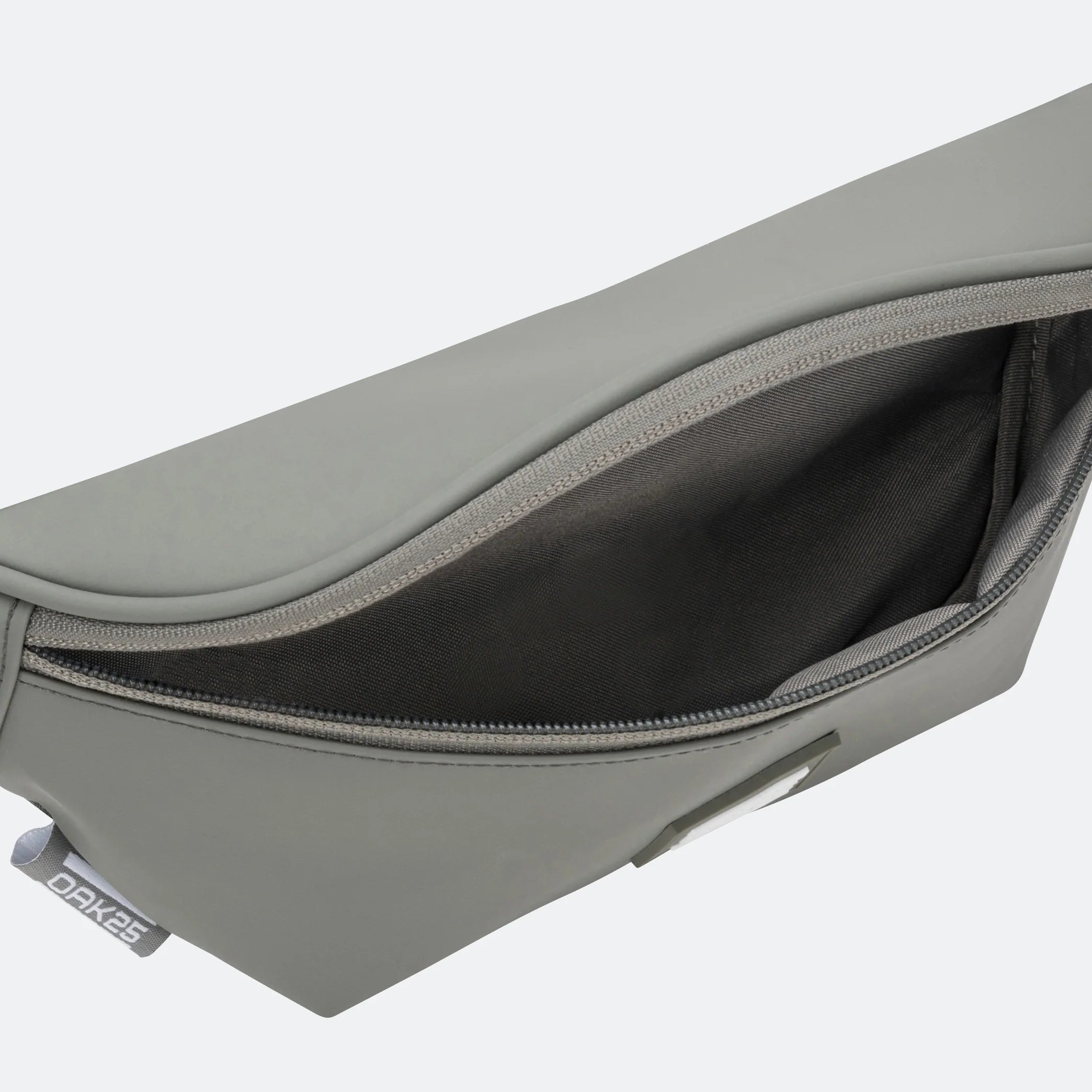 Eine Nahaufnahme einer geöffneten grauen Tasche mit Reißverschluss, die einen geräumigen schwarzen Innenraum zeigt. Auf der linken Seite des Beutels ist ein kleines Stoffschild mit dem Wort DAKINE zu sehen.