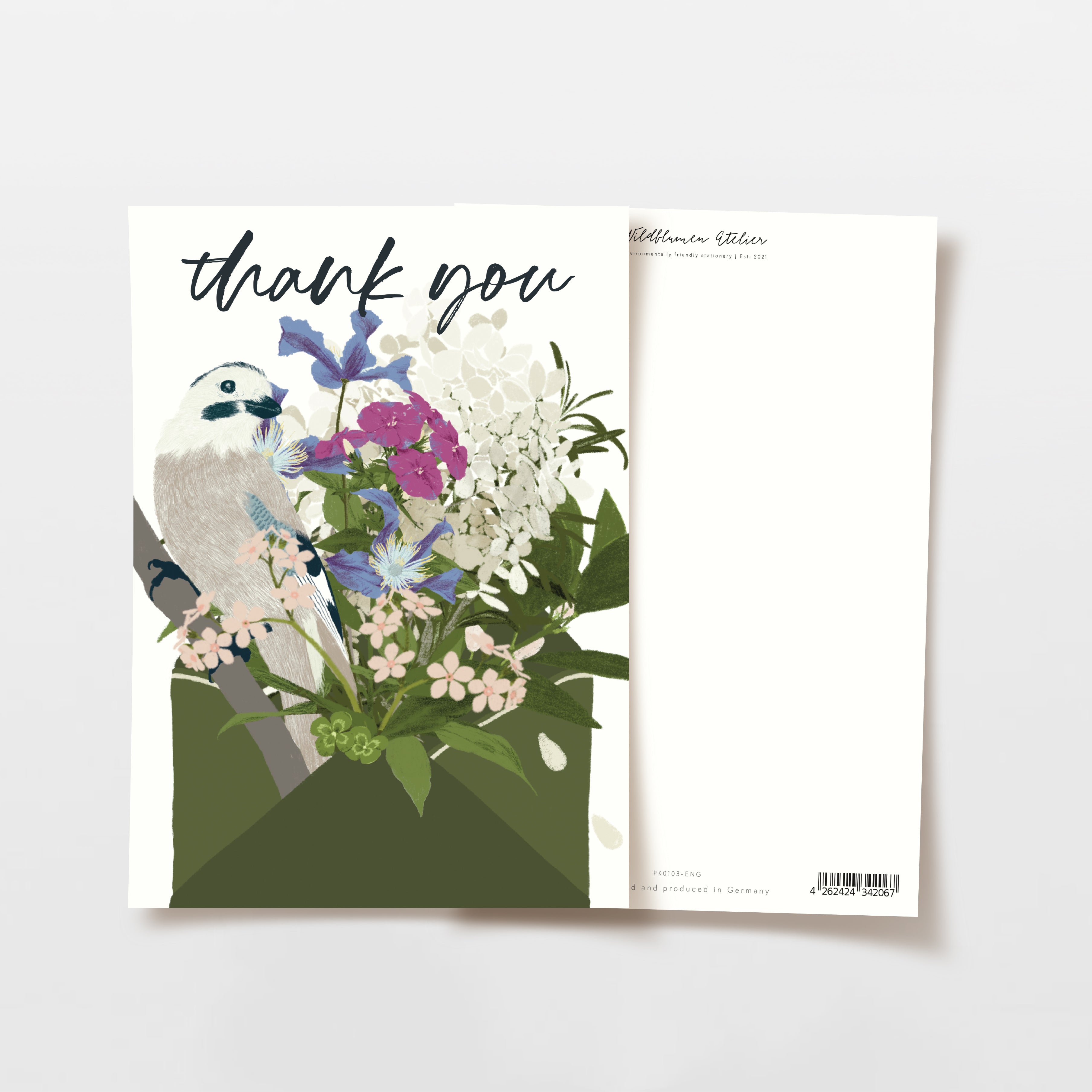 Eine Dankeskarte mit einem Blumenbouquet und einem kleinen weißen Vogel auf der Vorderseite. Die Worte "Danke" sind oben kursiv geschrieben. Die Karte bedeckt teilweise ihren schlichten weißen Umschlag.