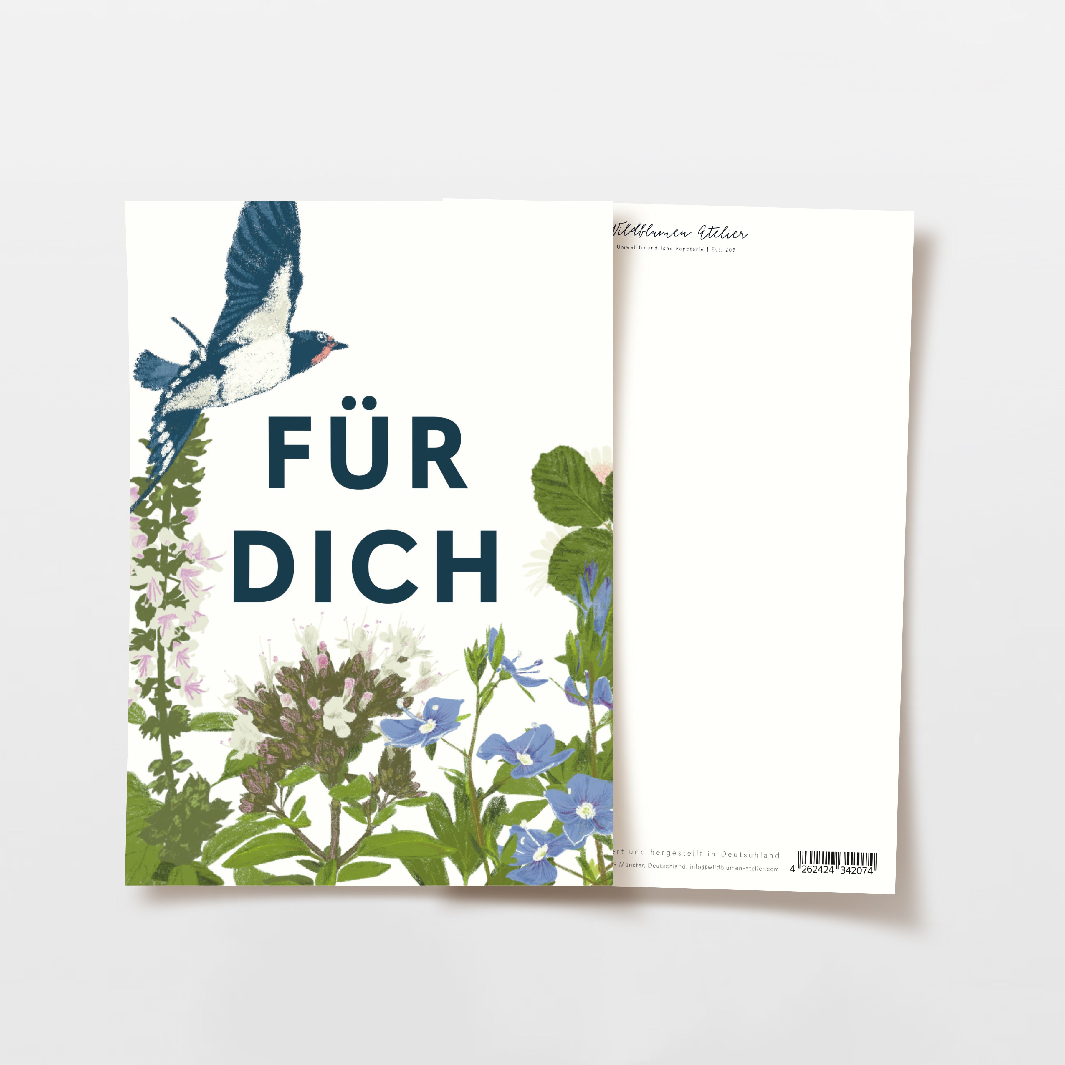 Eine Grußkarte mit den deutschen Worten FÜR DICH in fetten Buchstaben, umgeben von illustrierten Wildblumen und einer fliegenden Schwalbe. Die Karte befindet sich auf einem hellen Hintergrund, wobei die Rückseite teilweise sichtbar ist.