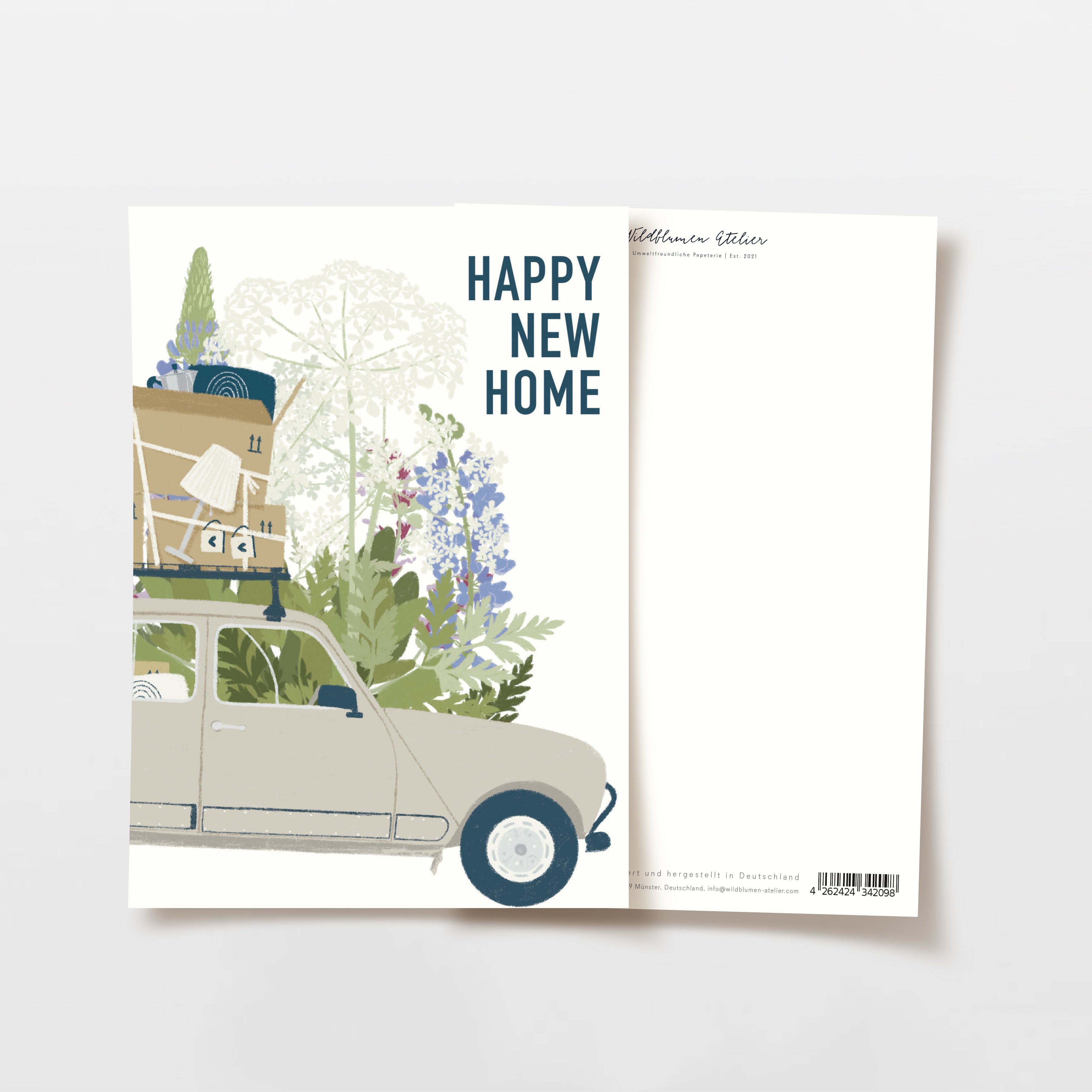Illustration eines Autos, das mit Kisten, Pflanzen und Möbeln auf dem Dach beladen ist, vor einem Hintergrund von hohen Grünpflanzen. Der Text darüber lautet "Happy New Home". Eine leere Postkarte ist teilweise hinter der illustrierten Karte sichtbar.