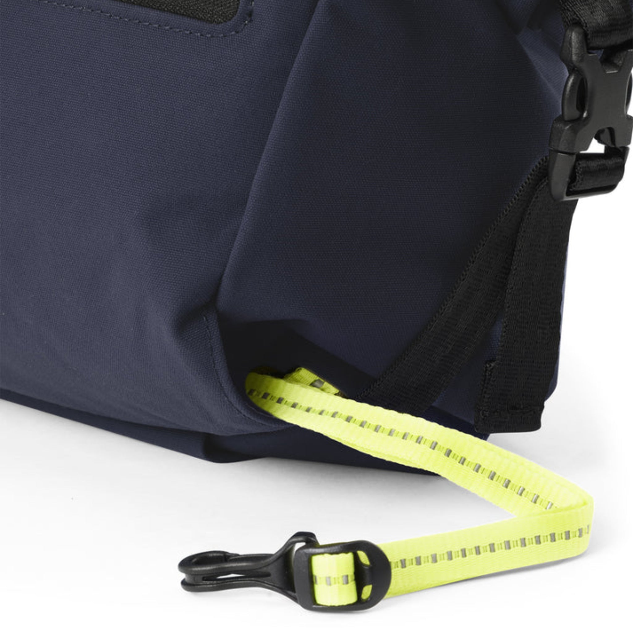 Nahaufnahme einer marineblauen Tasche mit einer schwarzen Schnalle und einem gelben Gurt mit reflektierenden Streifen und einem schwarzen Kunststoffclip am Ende.