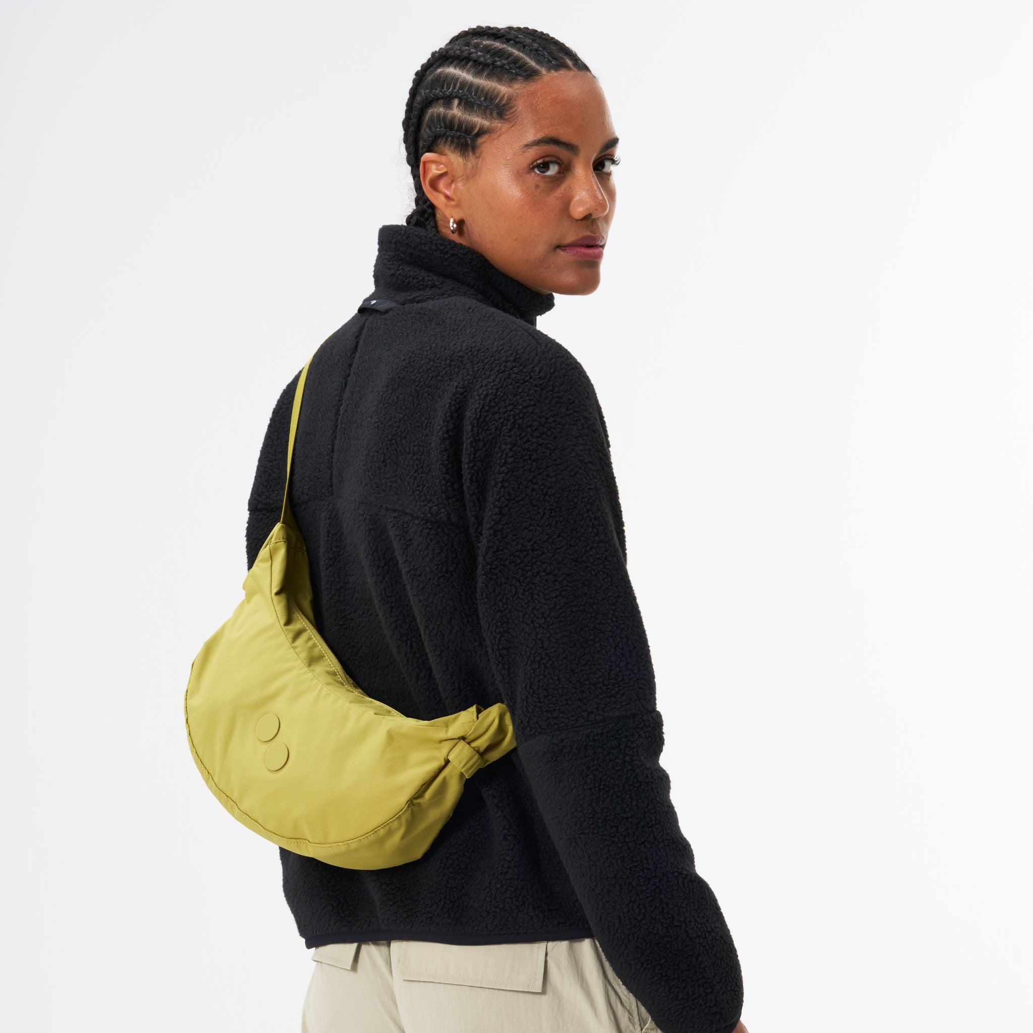 Person mit schwarzen Locken trägt schwarze Jacke und gelbe Umhängetasche, schaut über die Schulter.