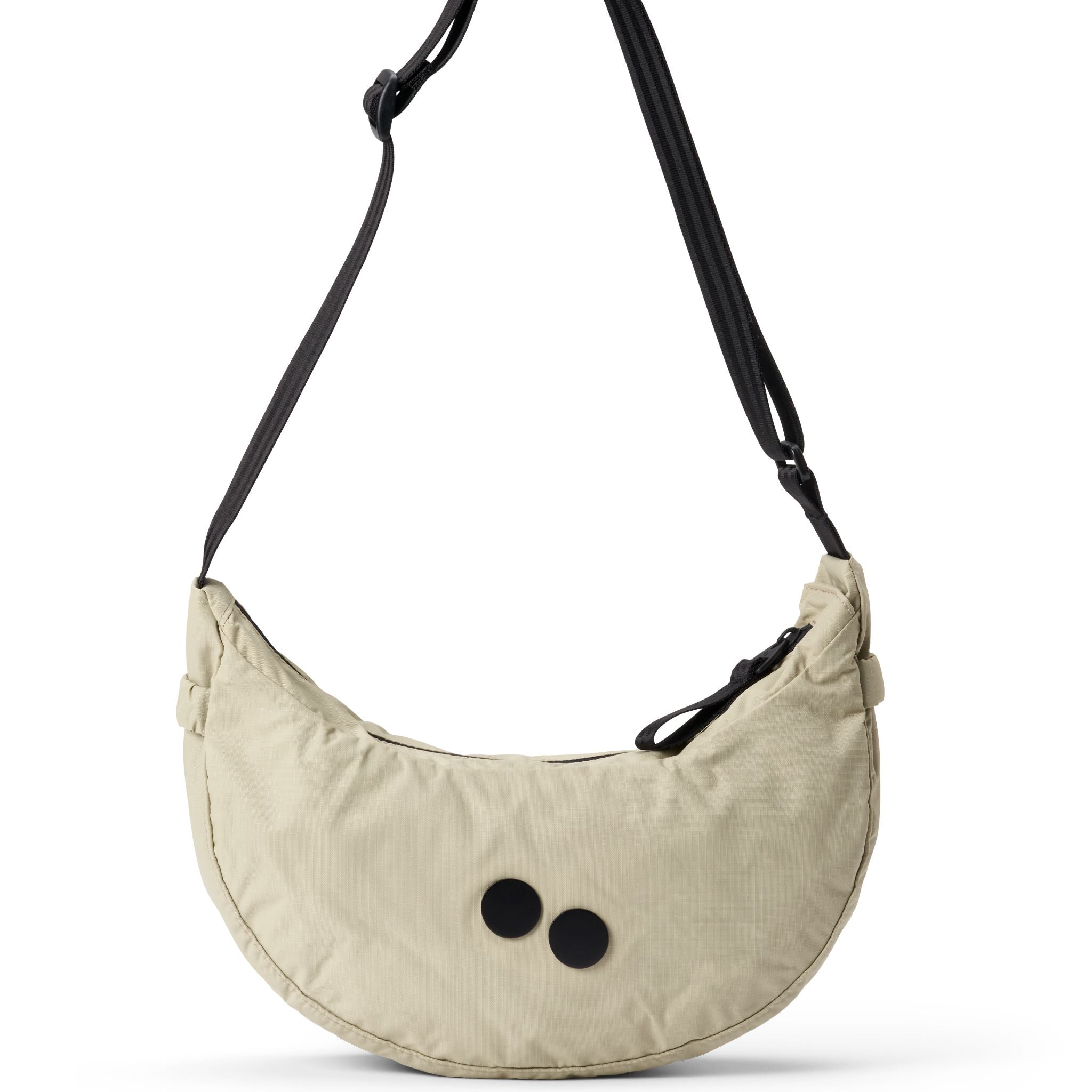 Beige Umhängetasche mit schwarzem Gurt und zwei schwarzen Punkten, halbkreisförmig und modern gestaltet.