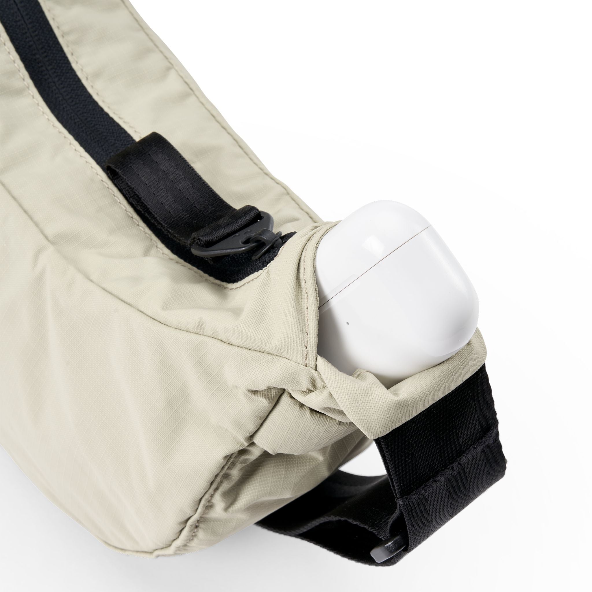 Beige Gürteltasche mit schwarzem Reißverschluss und weißem AirPods-Case in der Seitentasche.