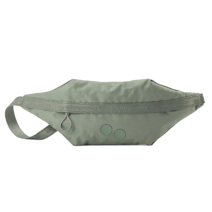 Eine salbeigrüne Hüfttasche mit Reißverschluss, verstellbarem Riemen und zwei kleinen farbigen Kreisen auf der Vorderseite. Die Tasche hat ein minimalistisches Design und dezente Nahtdetails.