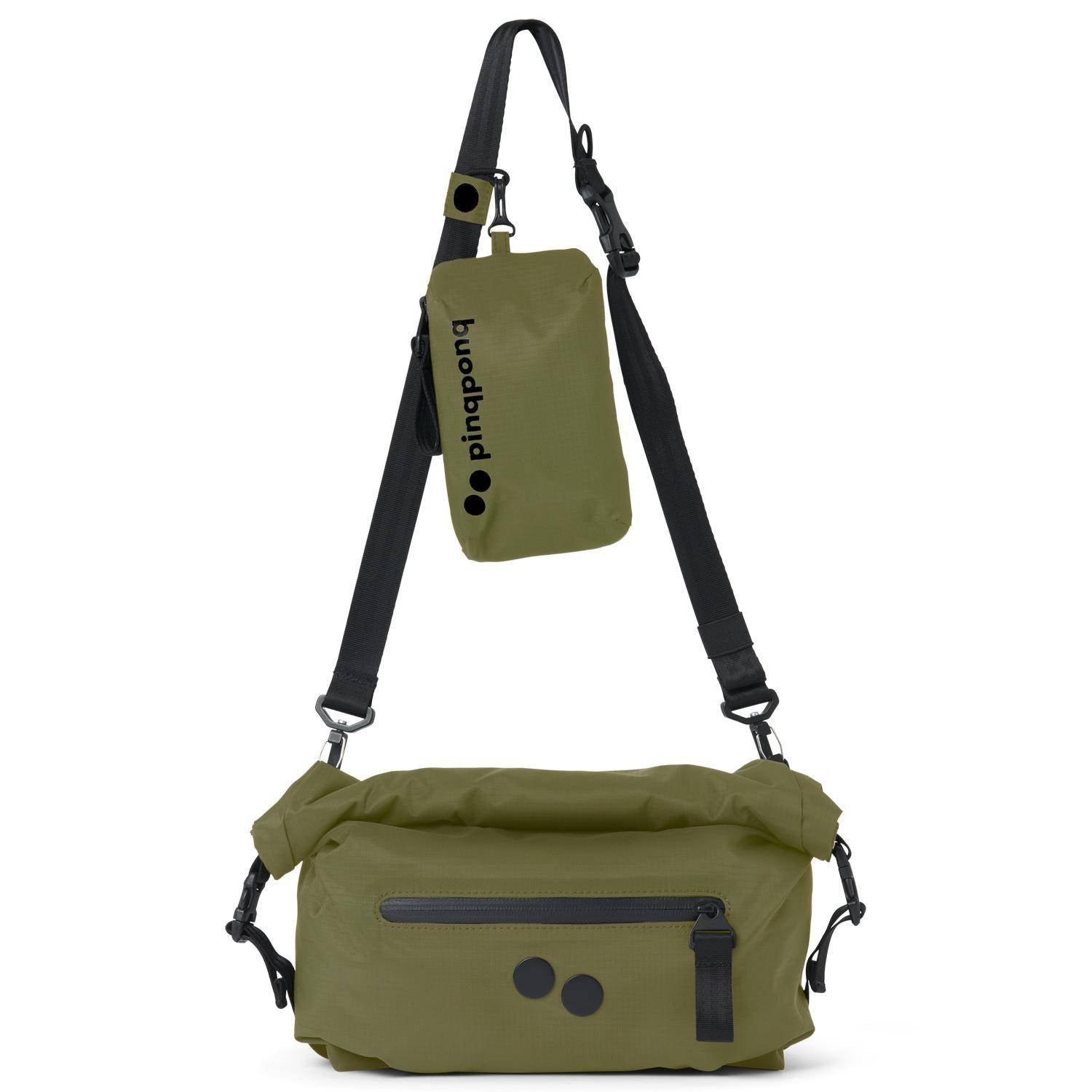 Eine olivgrüne Umhängetasche mit schwarzen Trägern, einer Reißverschlusstasche auf der Vorderseite und zwei schwarzen runden Akzenten. Ein passender, abnehmbarer Beutel mit schwarzem Text hängt am Riemen.