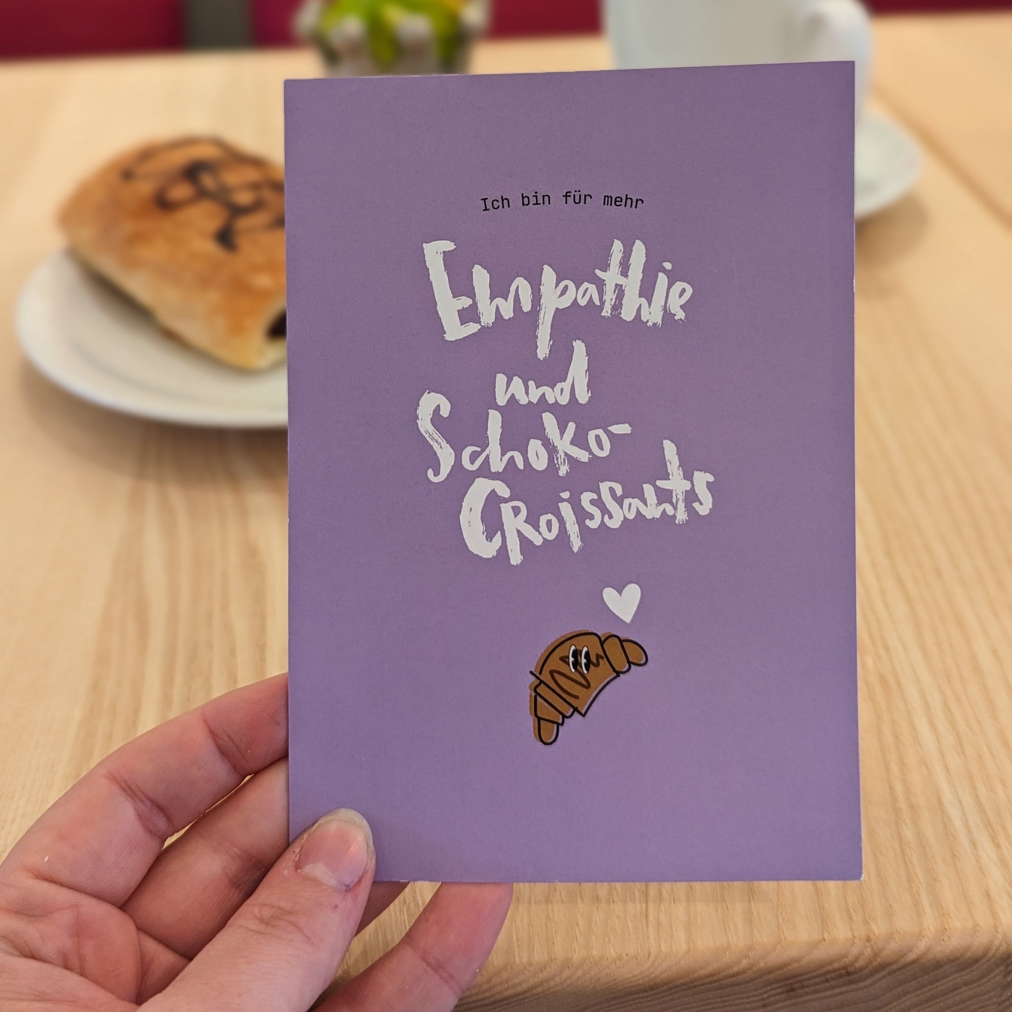 Lila Karte mit der Aufschrift "Ich bin für mehr Empathie und Schoko-Croissants" und einem gezeichneten Croissant.