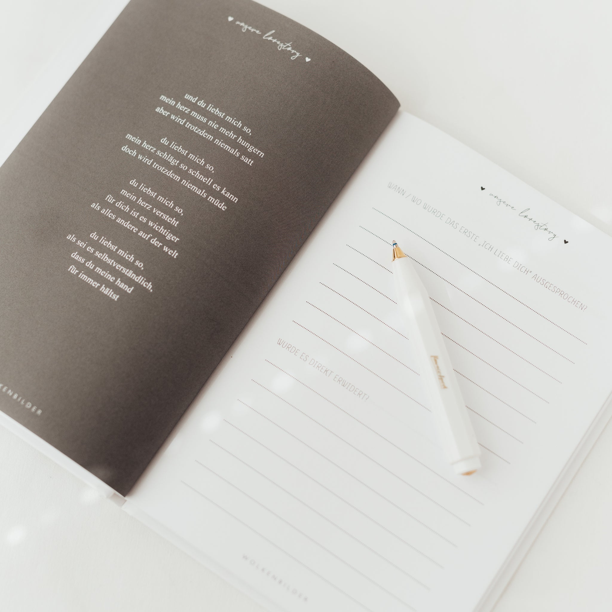 Aufgeschlagenes Notizbuch mit einem Gedicht auf einer Seite und leeren Zeilen auf der anderen, daneben ein weißer Stift.
