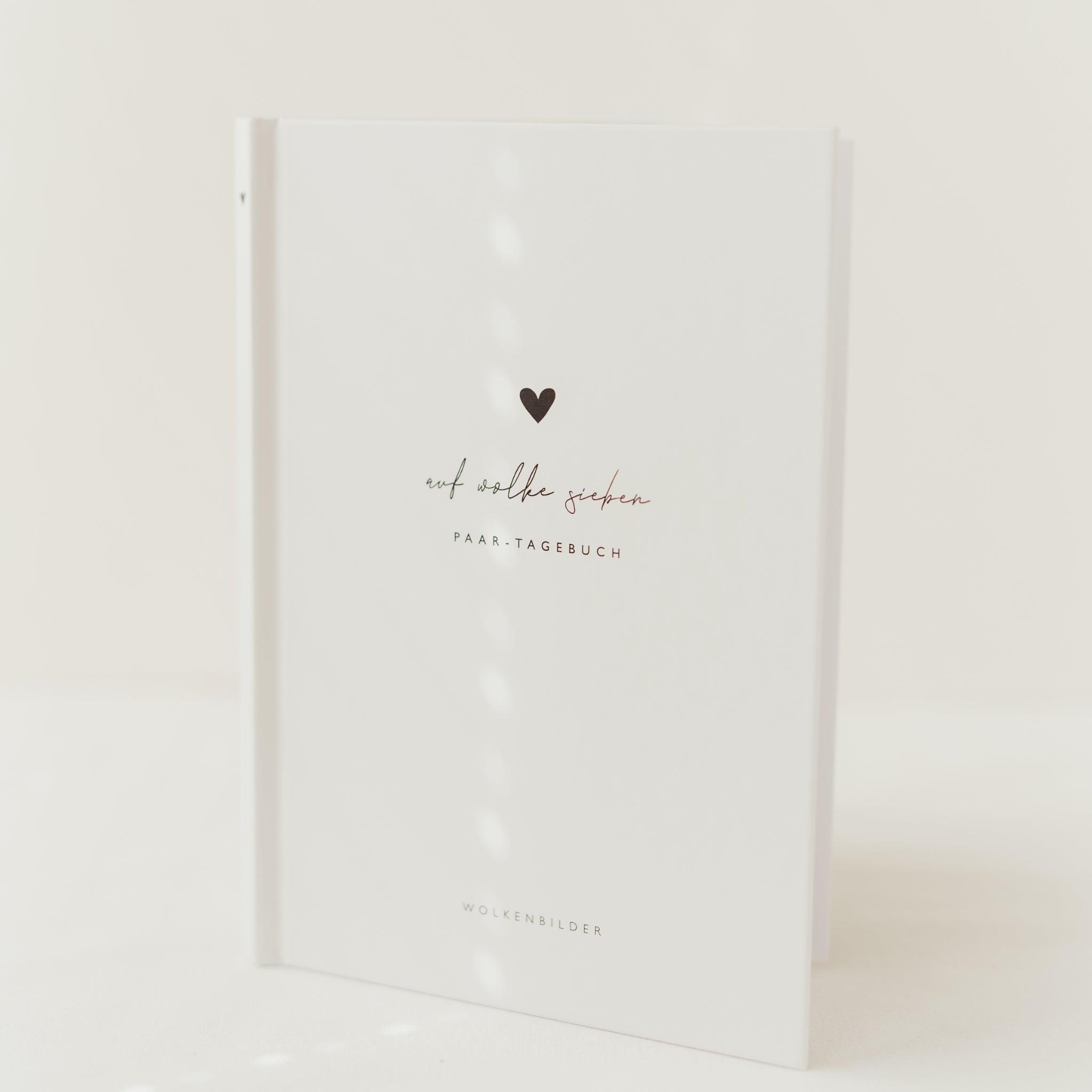 Weißes Buch mit Herz und der Aufschrift "auf wolke sieben - PAAR-TAGEBUCH" auf dem Cover.