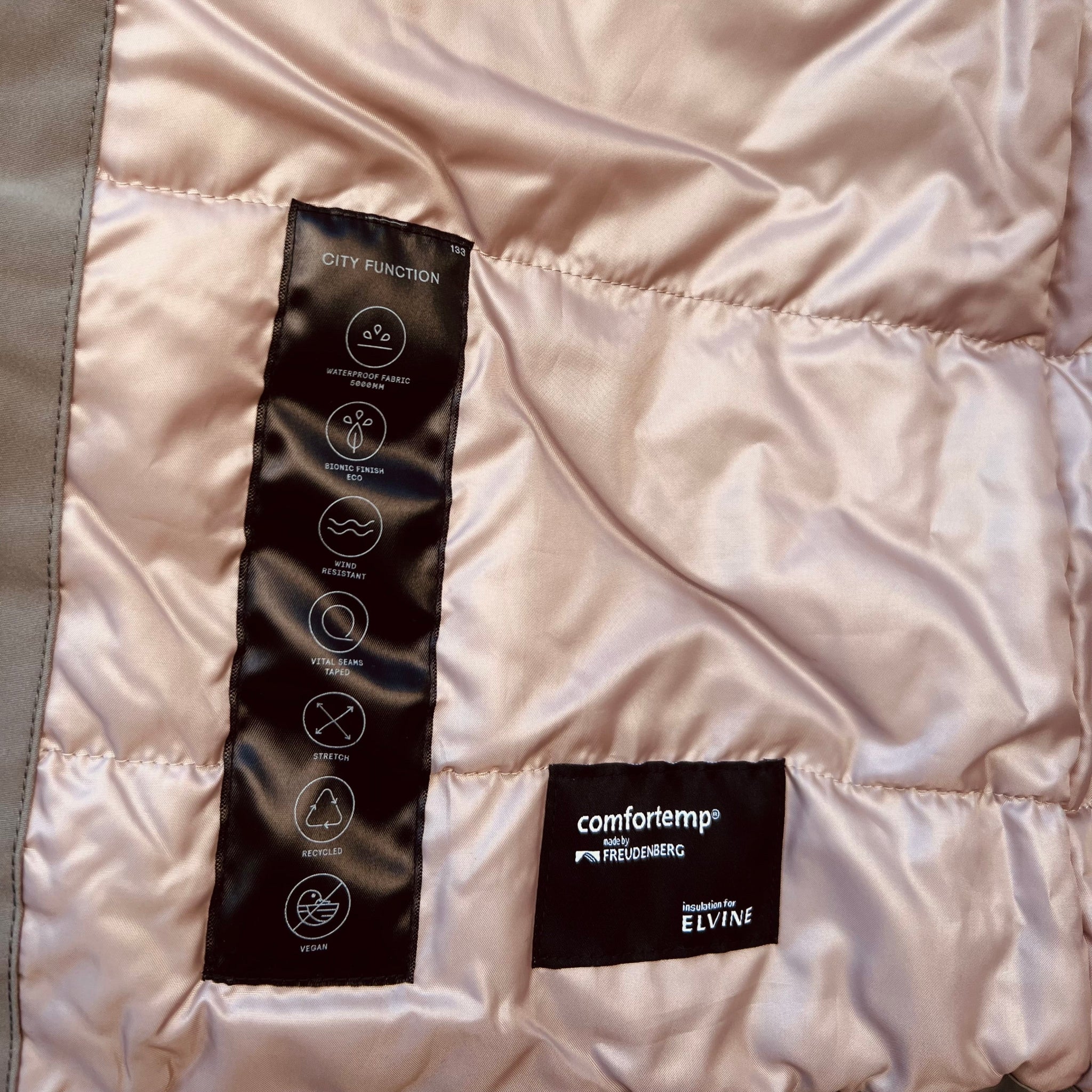 Innenfutter einer Jacke mit Etiketten, die wasserdicht, winddicht, dehnbar, recycelt und vegan beschreiben.