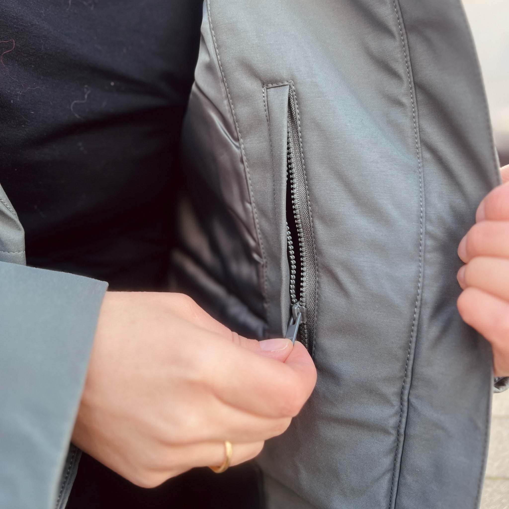 Eine Person öffnet den Reißverschluss einer grauen Jackentasche mit der Hand.