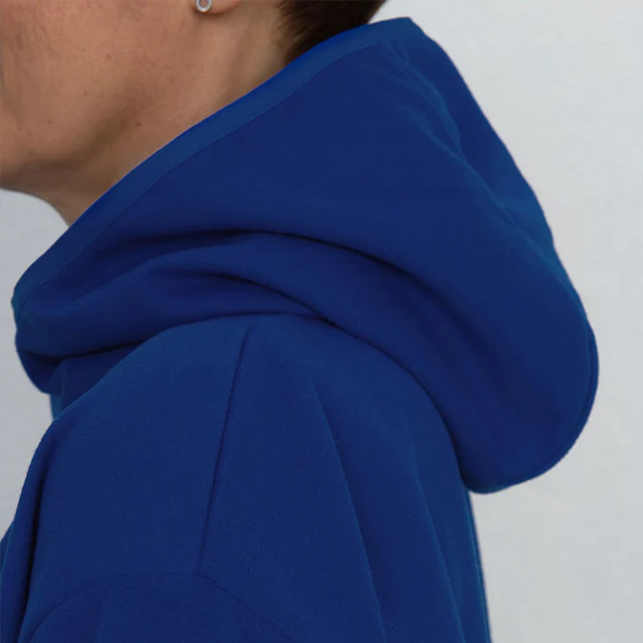 Nahaufnahme einer Person, die ein königsblaues Sweatshirt mit Kapuze trägt, wobei die Kapuze über die Schultern gezogen ist und einen Teil des Gesichts und der Ohren zeigt.