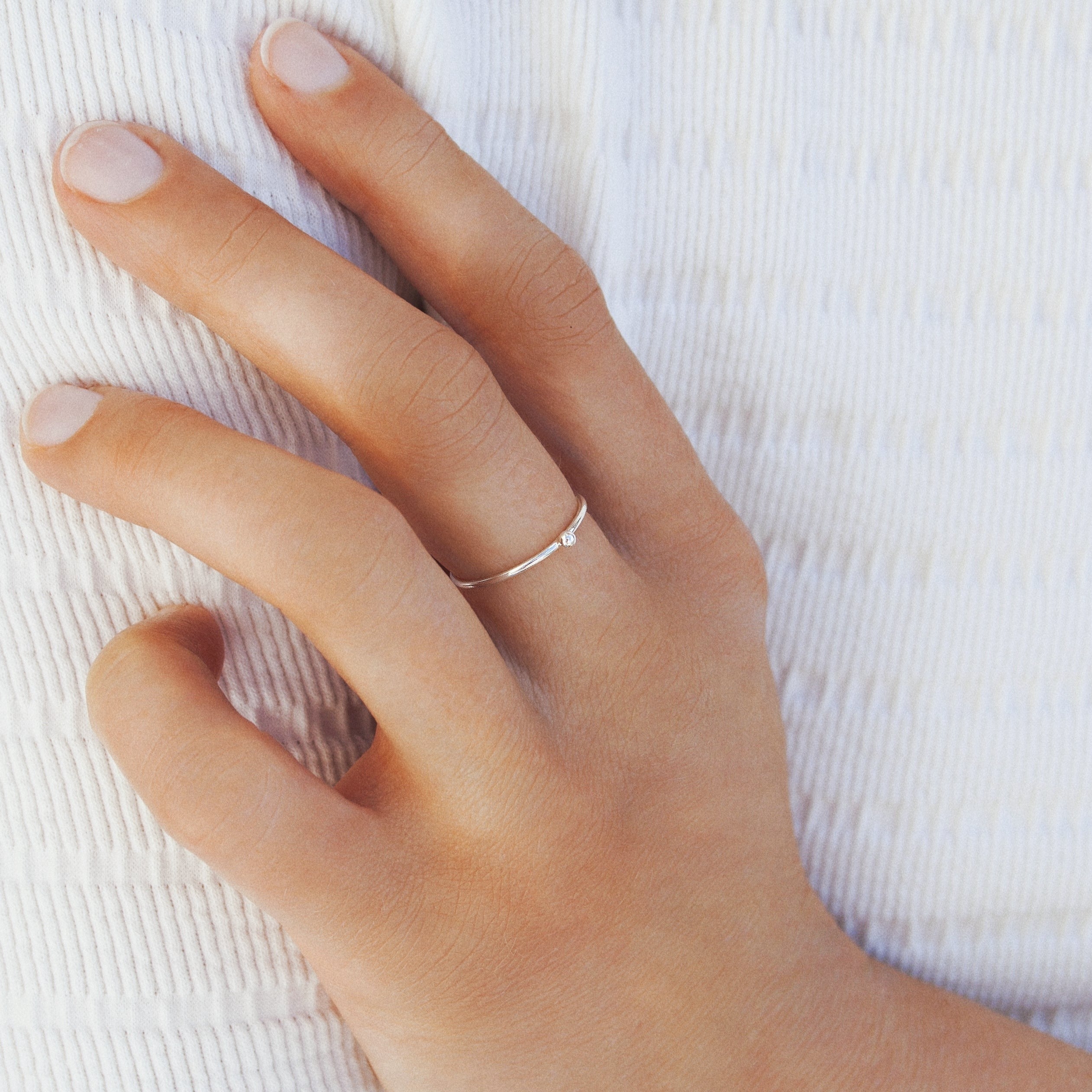 Hand mit zartem, silbernen Ring auf weißem Stoff.