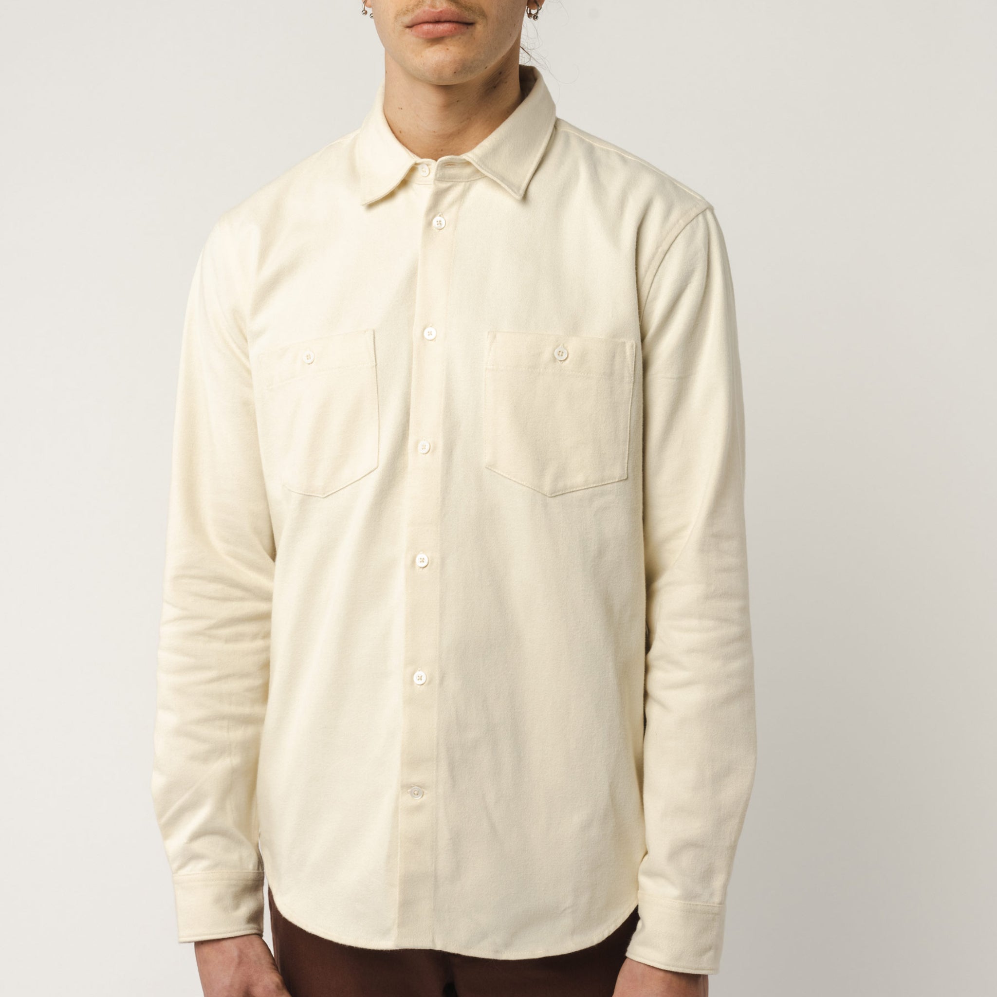 Person in beigem Hemd mit Brusttaschen vor neutralem Hintergrund.