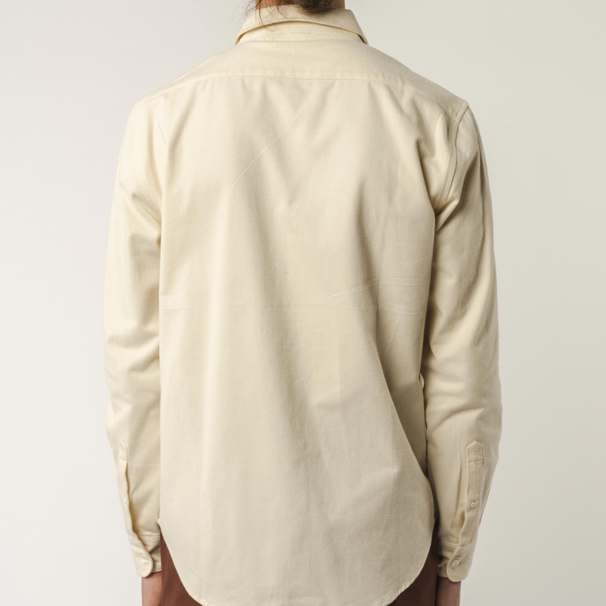 Person in beigem Hemd, von hinten fotografiert, vor neutralem Hintergrund.