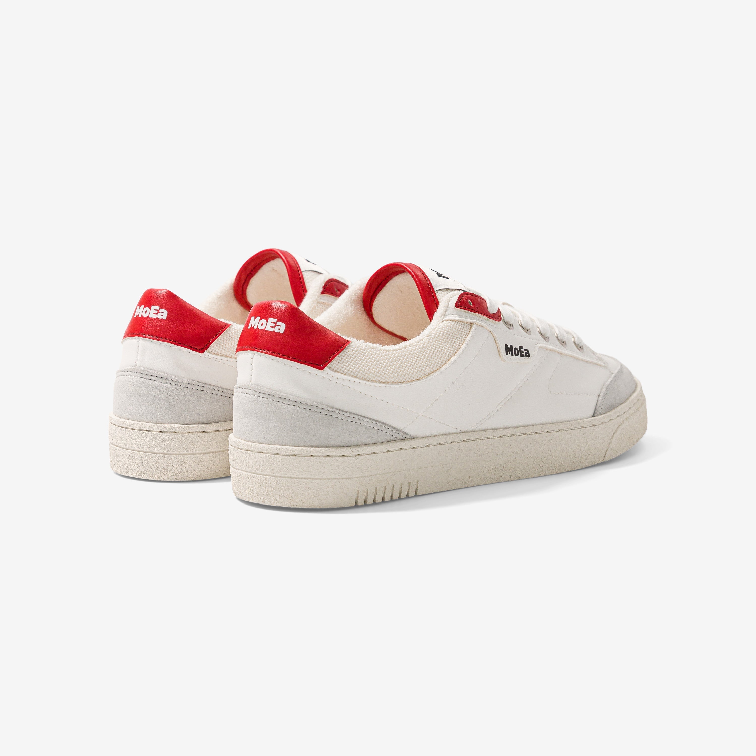 Ein Paar weiße Sneakers mit hellgrauen Details, beigen Sohlen und roten Fersenakzenten. Der Markenname MoEa erscheint an der Seite und an der Ferse. Die Schuhe sind auf einem schlichten weißen Hintergrund platziert.