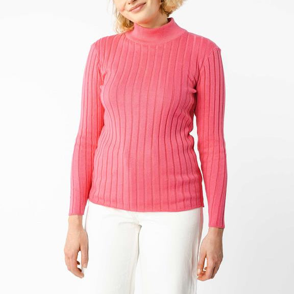 Eine Person, die einen langärmeligen, gerippten, rosa Rollkragenpullover und eine weiße Hose trägt, steht vor einem schlichten weißen Hintergrund. Ihr Gesicht ist teilweise außerhalb des Rahmens.