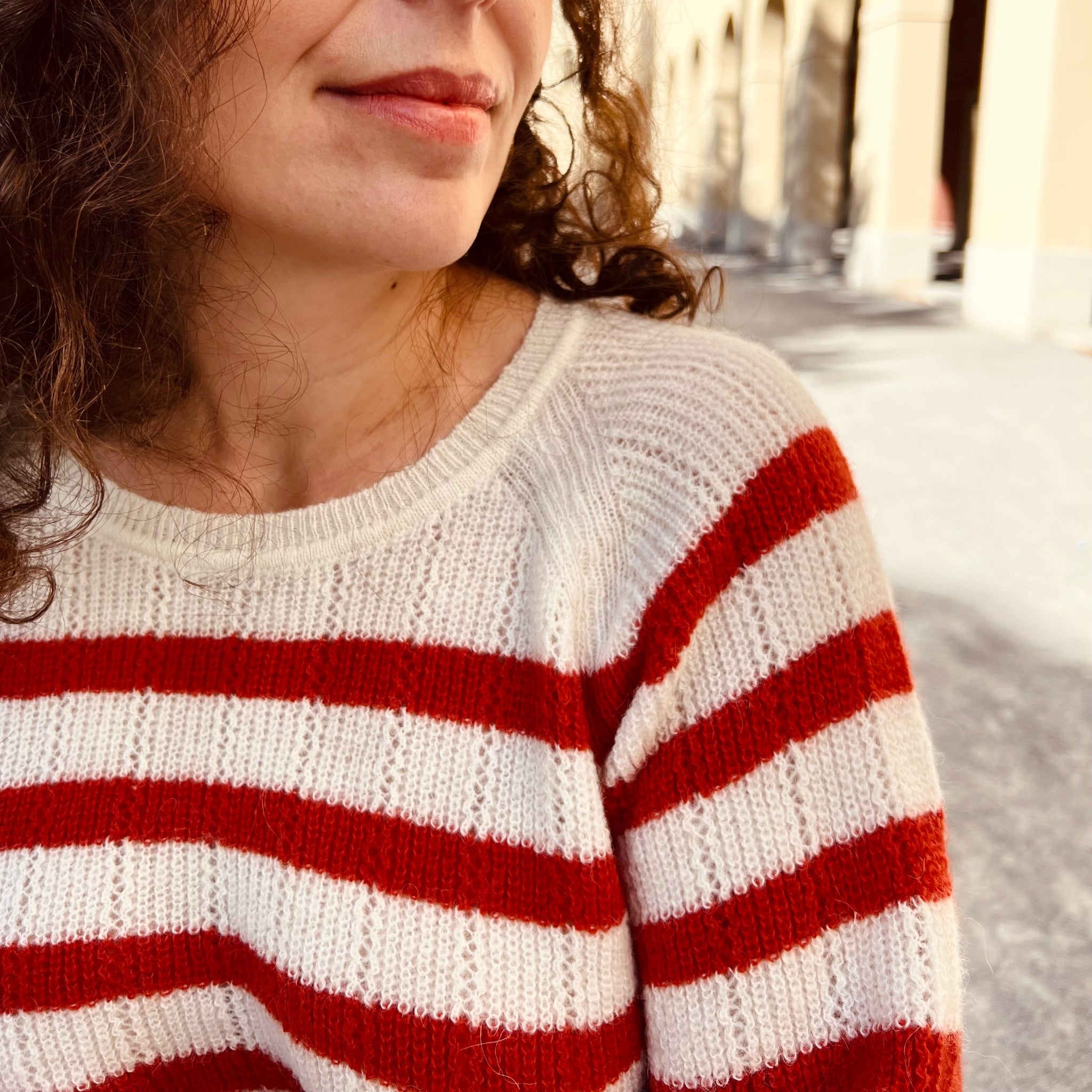 Eine Frau in einem Pullover mit roten und weißen Streifen, im Freien, teilweise sichtbar.