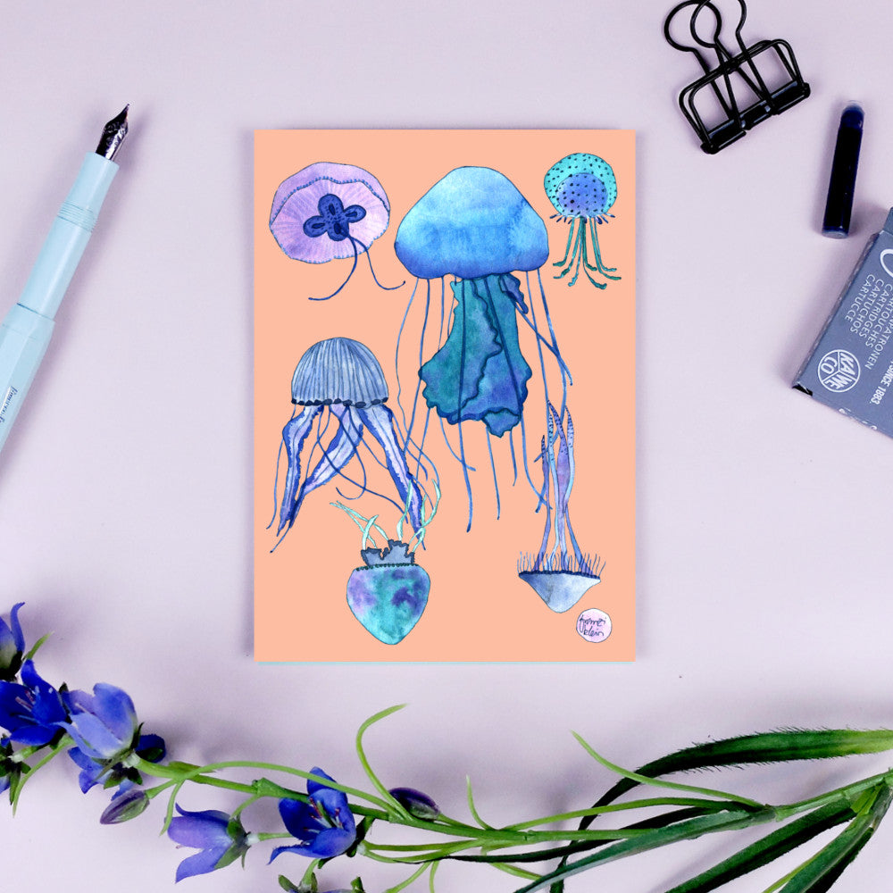 Illustration von bunten Quallen auf einem beigefarbenen Hintergrund, daneben liegen eine Feder, Blumen und Büroklammern.