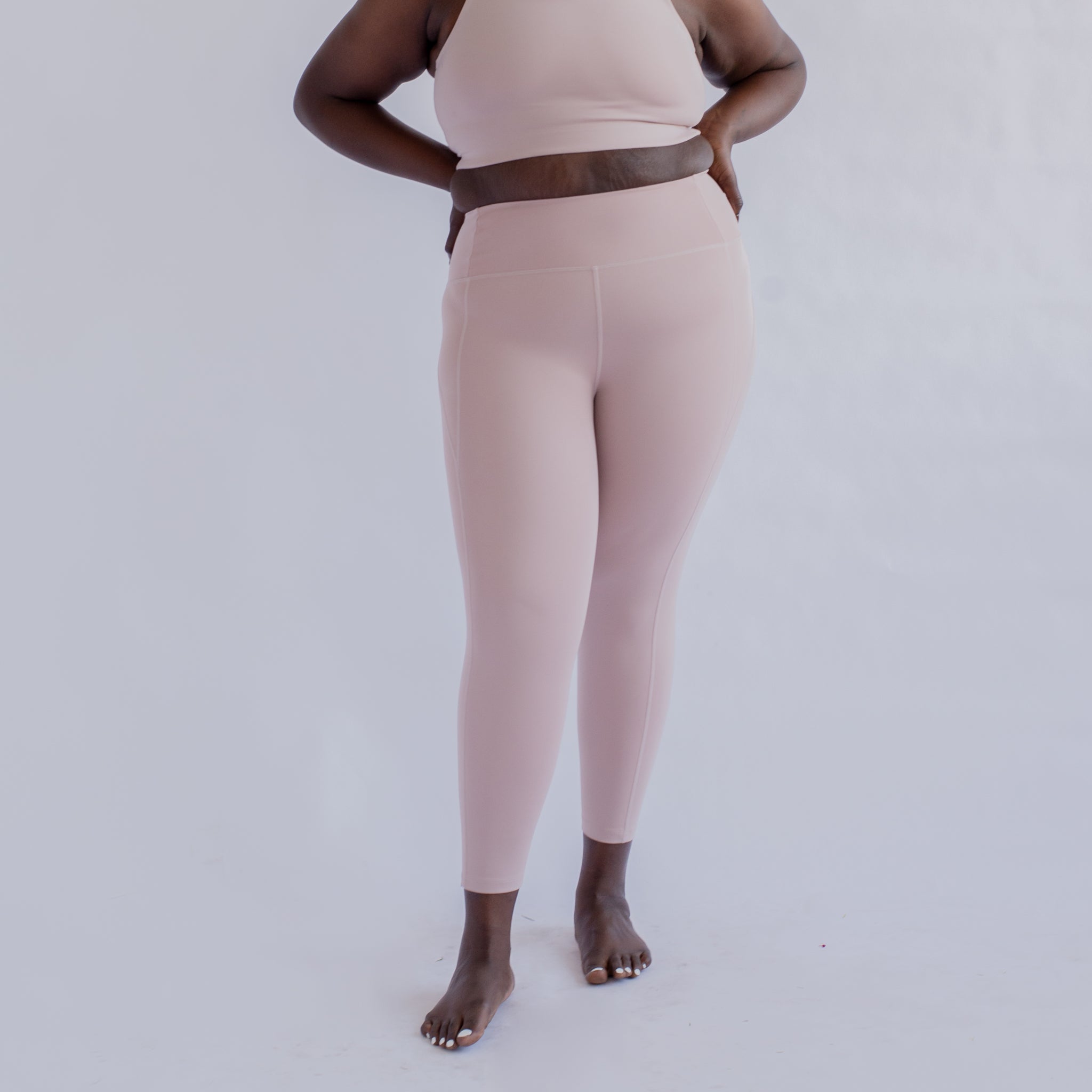 Eine Person in rosafarbener Sportbekleidung steht vor einem weißen Hintergrund und hält ihre Taille.