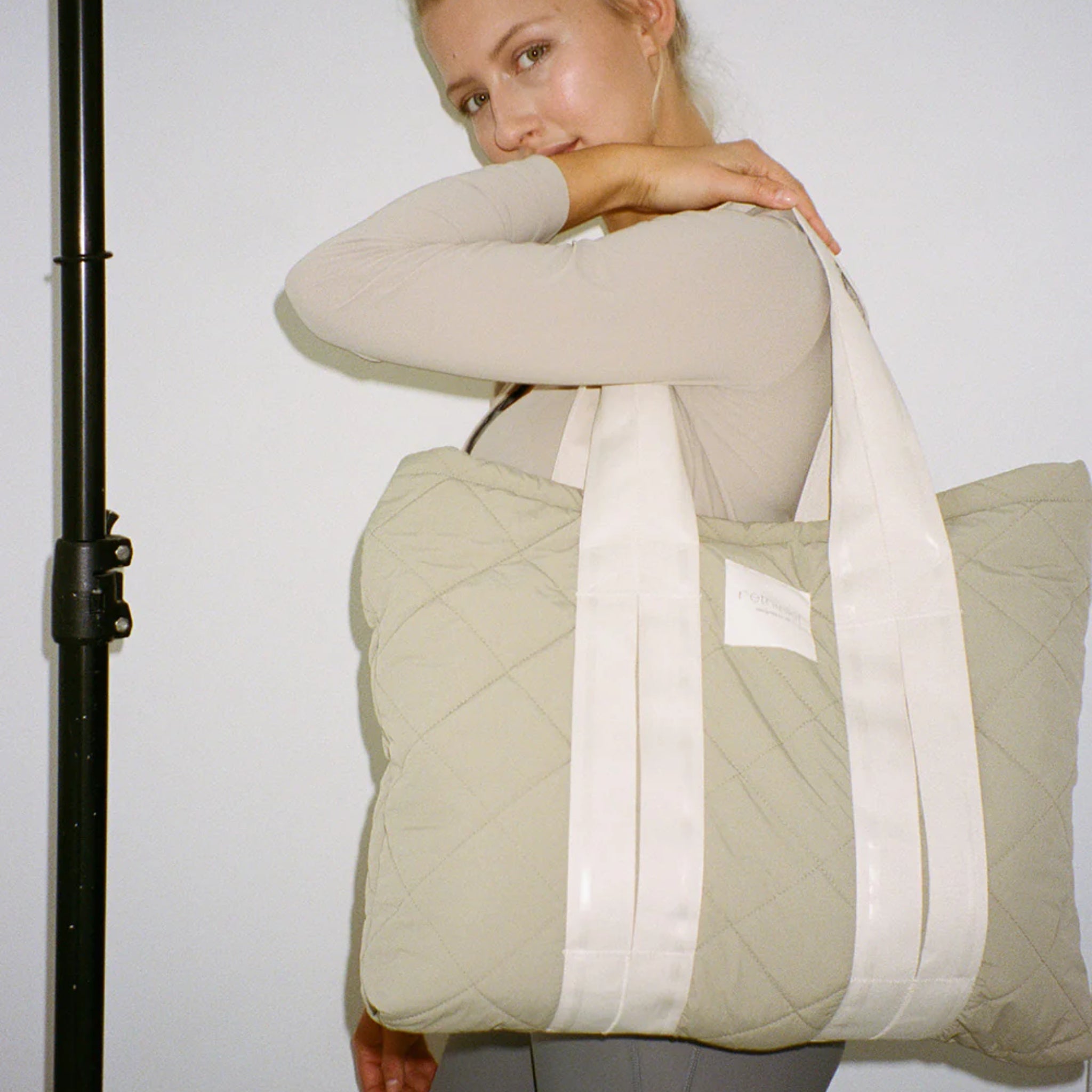 Eine Frau trägt eine große, gesteppte beigefarbene Tasche mit weißen Trägern auf der Schulter.