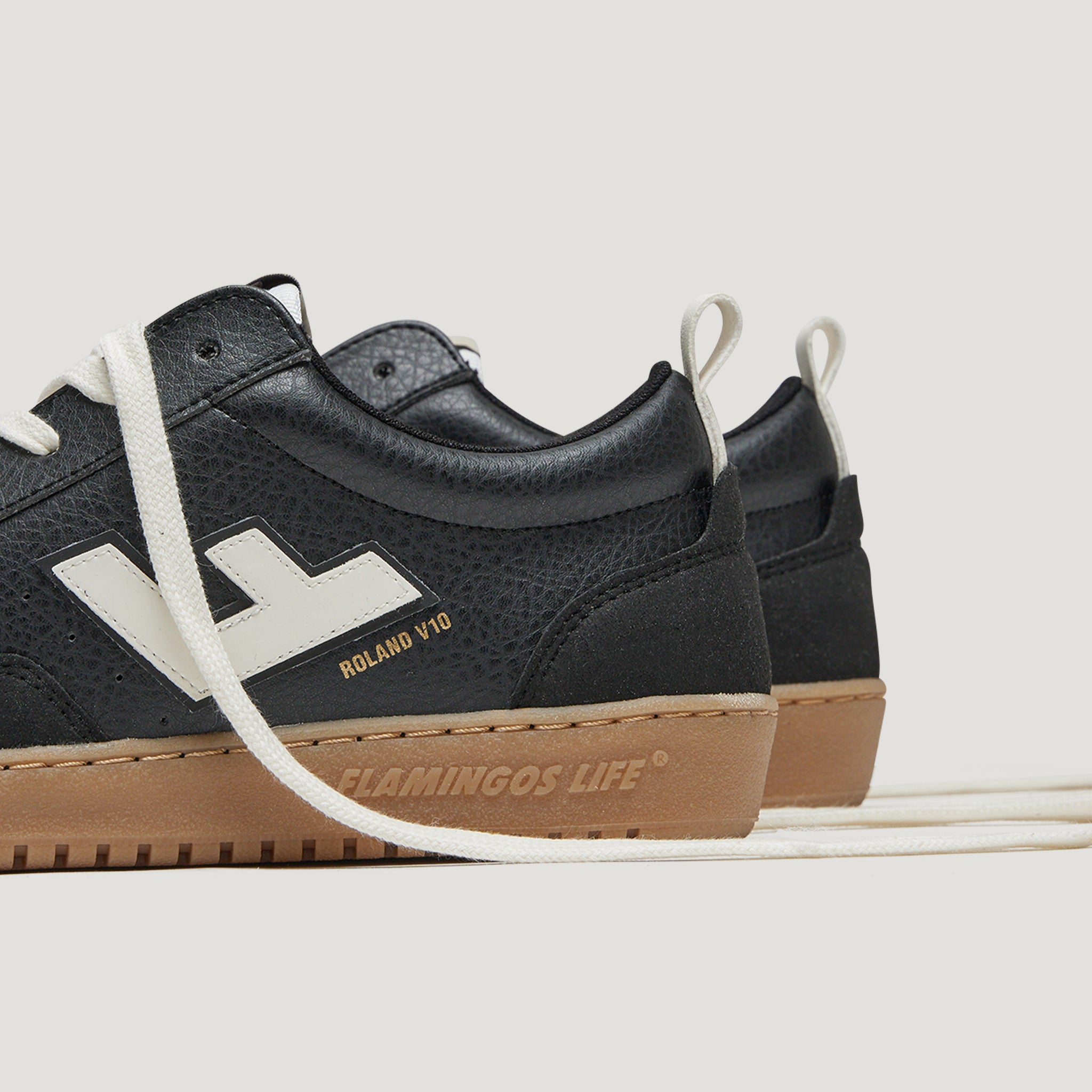 Schwarze Sneaker mit weißem Logo und Schriftzug "ROLAND V10", hellbrauner Sohle und weißen Schnürsenkeln.