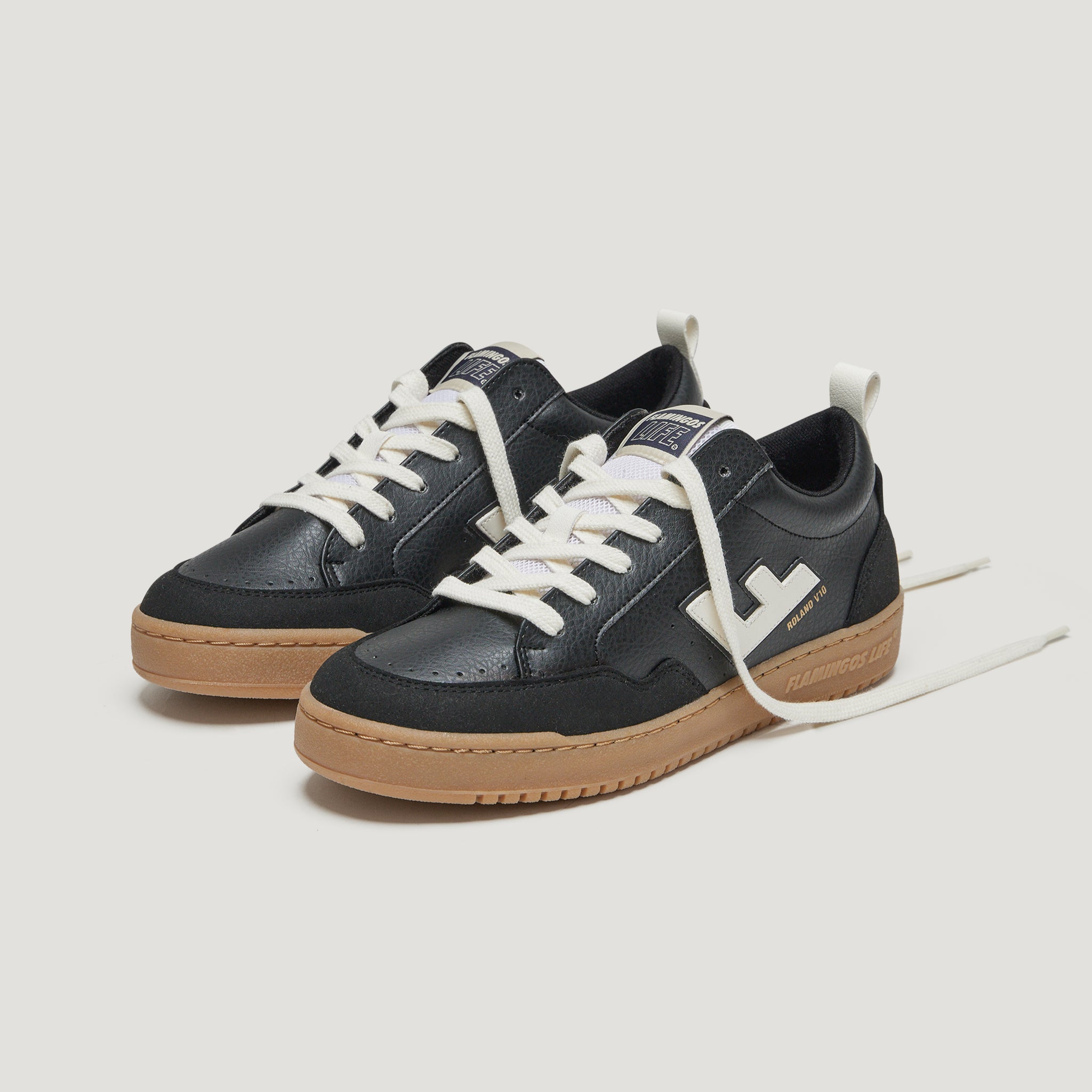 Schwarze Sneaker mit weißer Sohle und weißen Schnürsenkeln auf hellem Hintergrund.