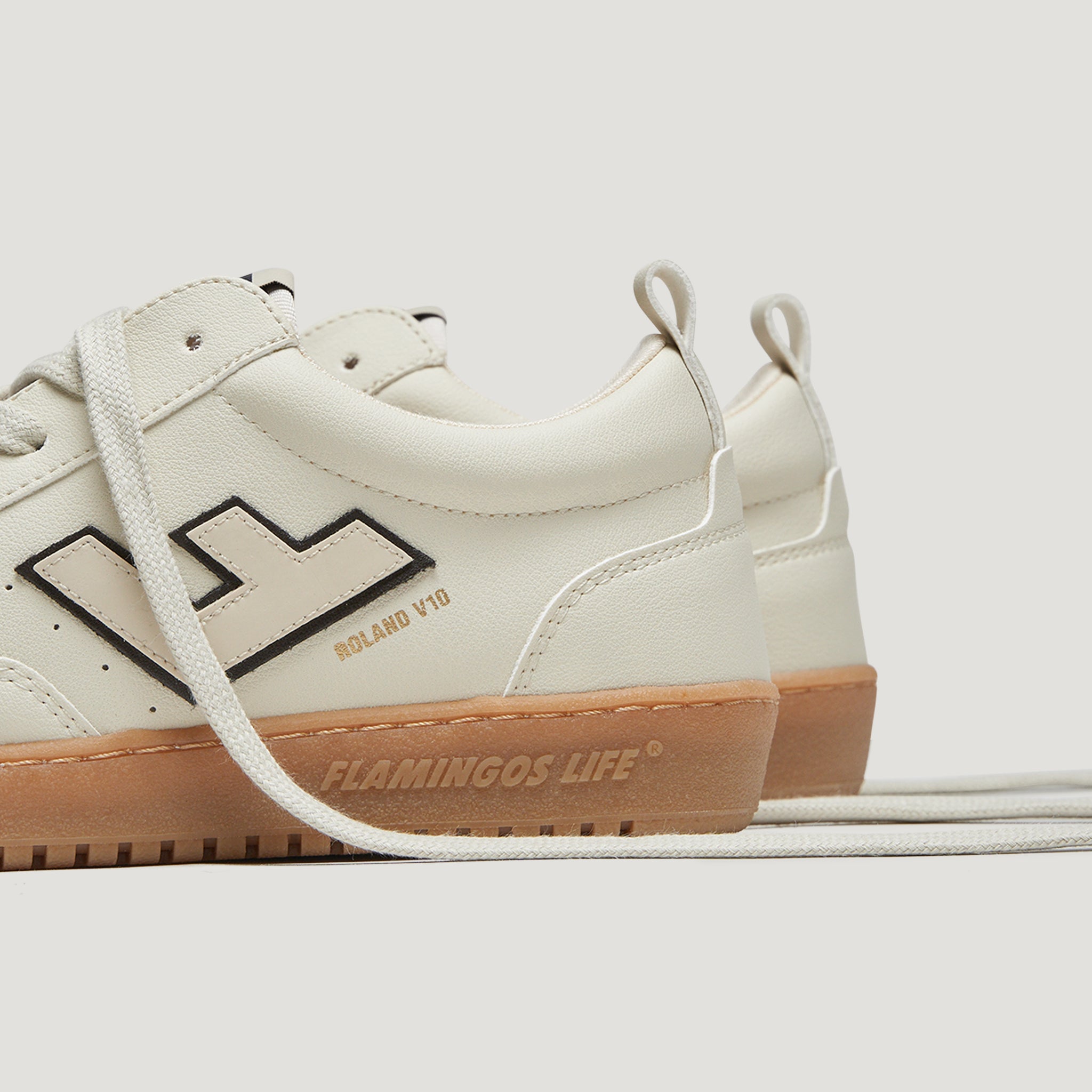 Weiße Sneakers mit brauner Sohle, seitliche Beschriftung "ROLAND V10" und "FLAMINGOS LIFE", sichtbares Logo seitlich.
