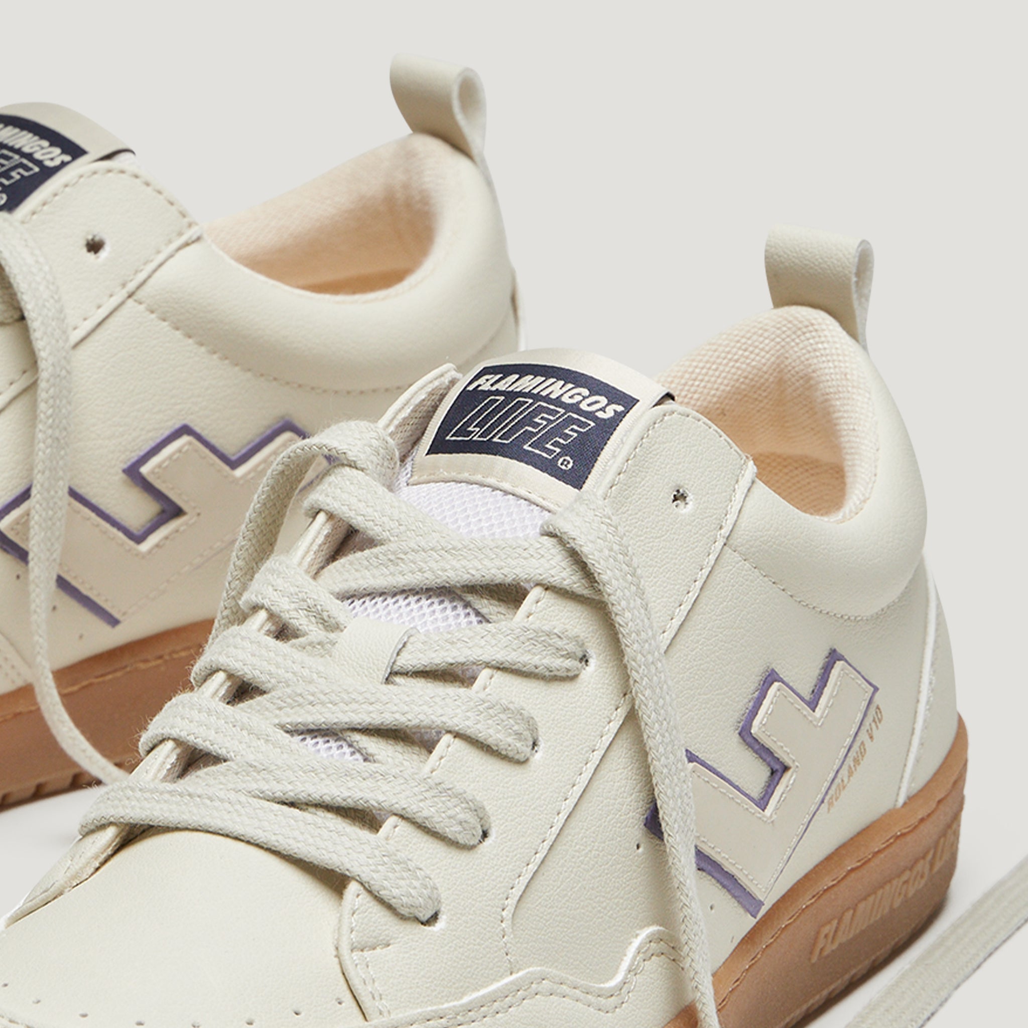 Nahaufnahme von cremefarbenen Sneakern mit weißem Logo und Details in Lila und Beige.