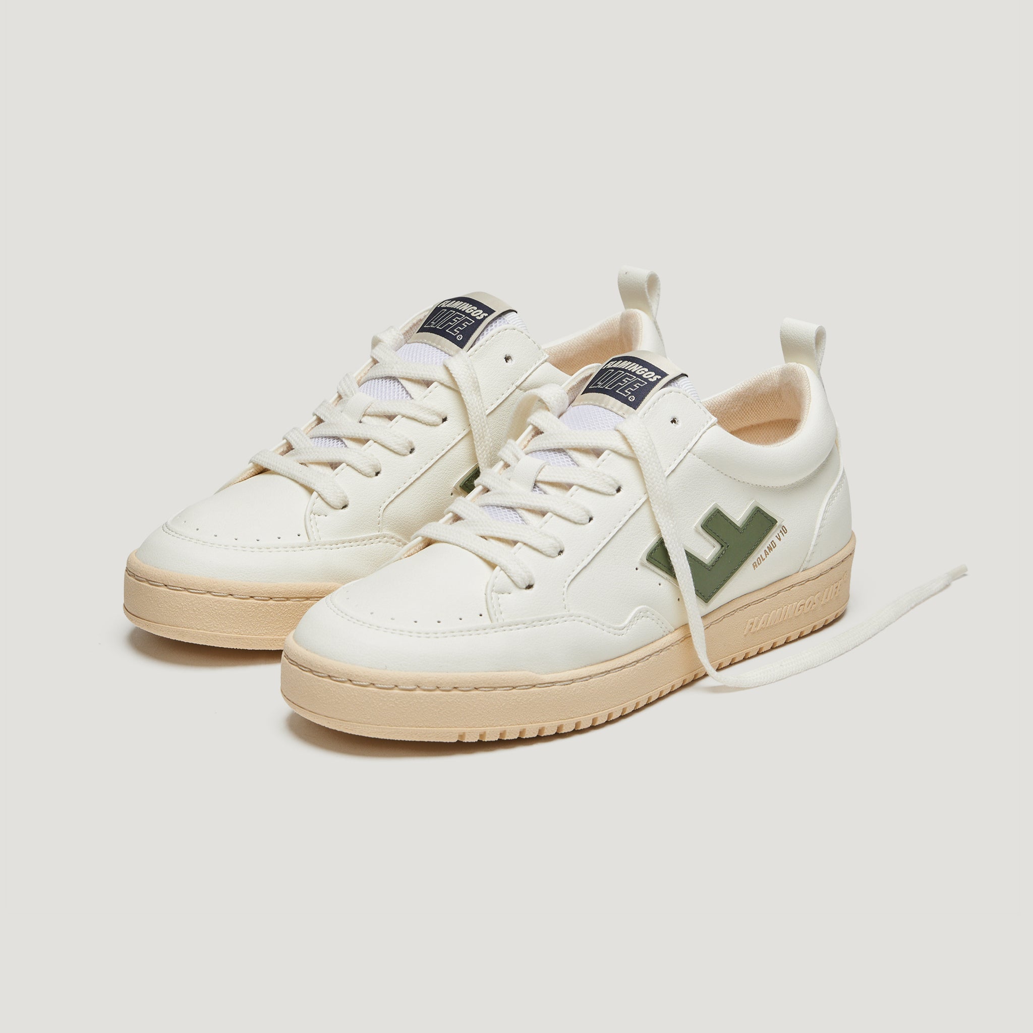 Weiße Sneaker mit brauner Sohle und grünem Seitenlogo, auf einer weißen Oberfläche platziert.