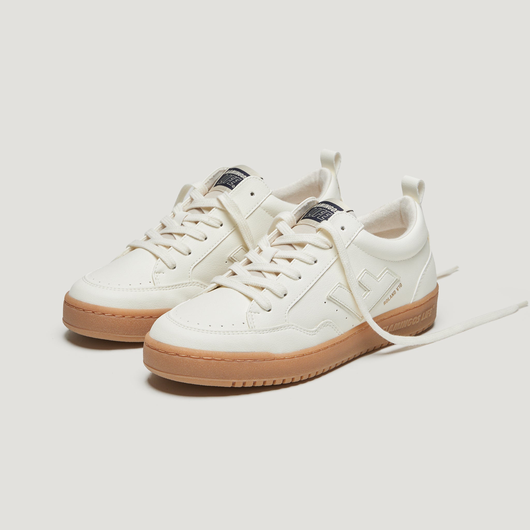 Weiße Sneaker mit hellbrauner Sohle und lässig gebundenen Schnürsenkeln auf einem hellen Hintergrund.