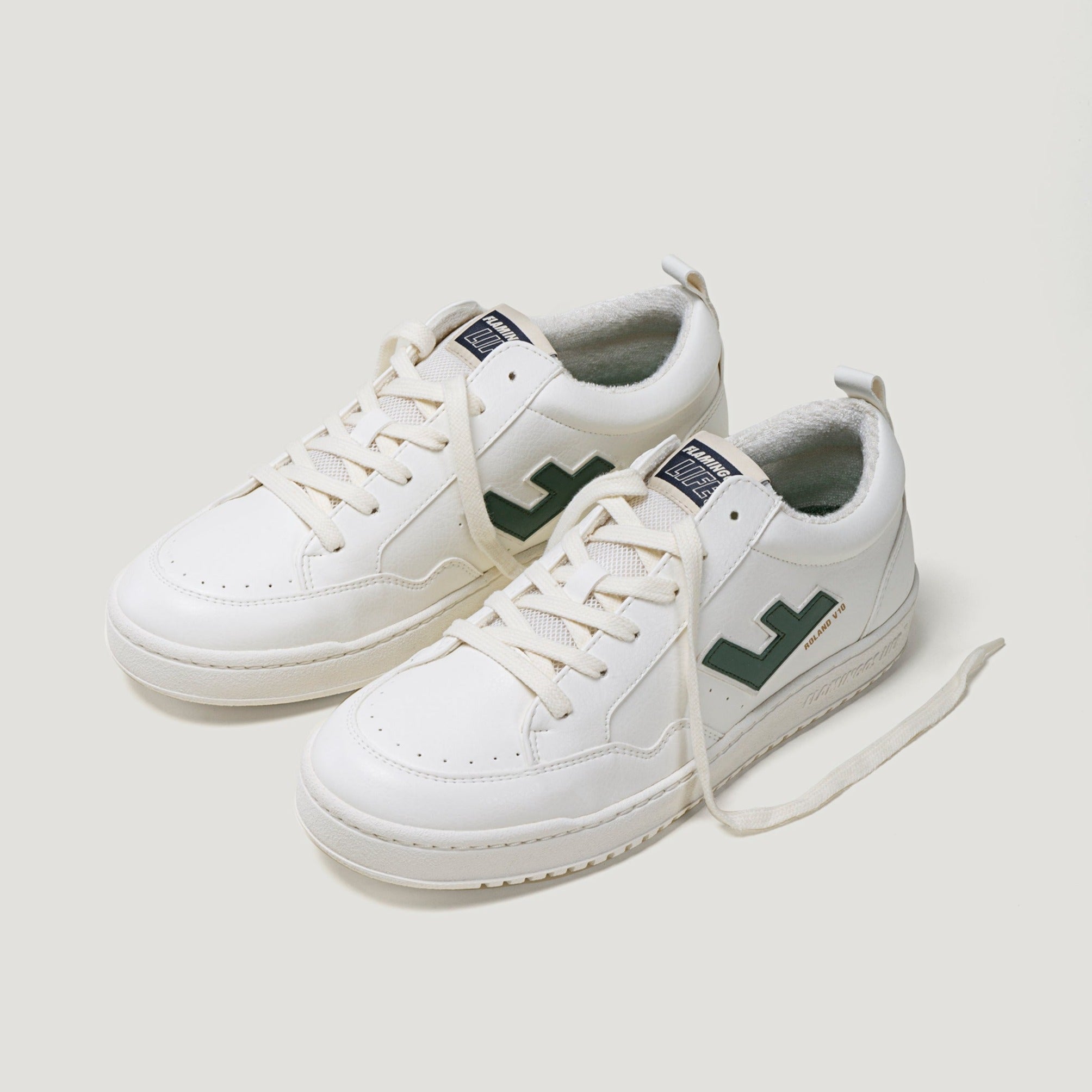 Weiße Turnschuhe mit grünen Details, schräg auf einem neutralen Hintergrund fotografiert.