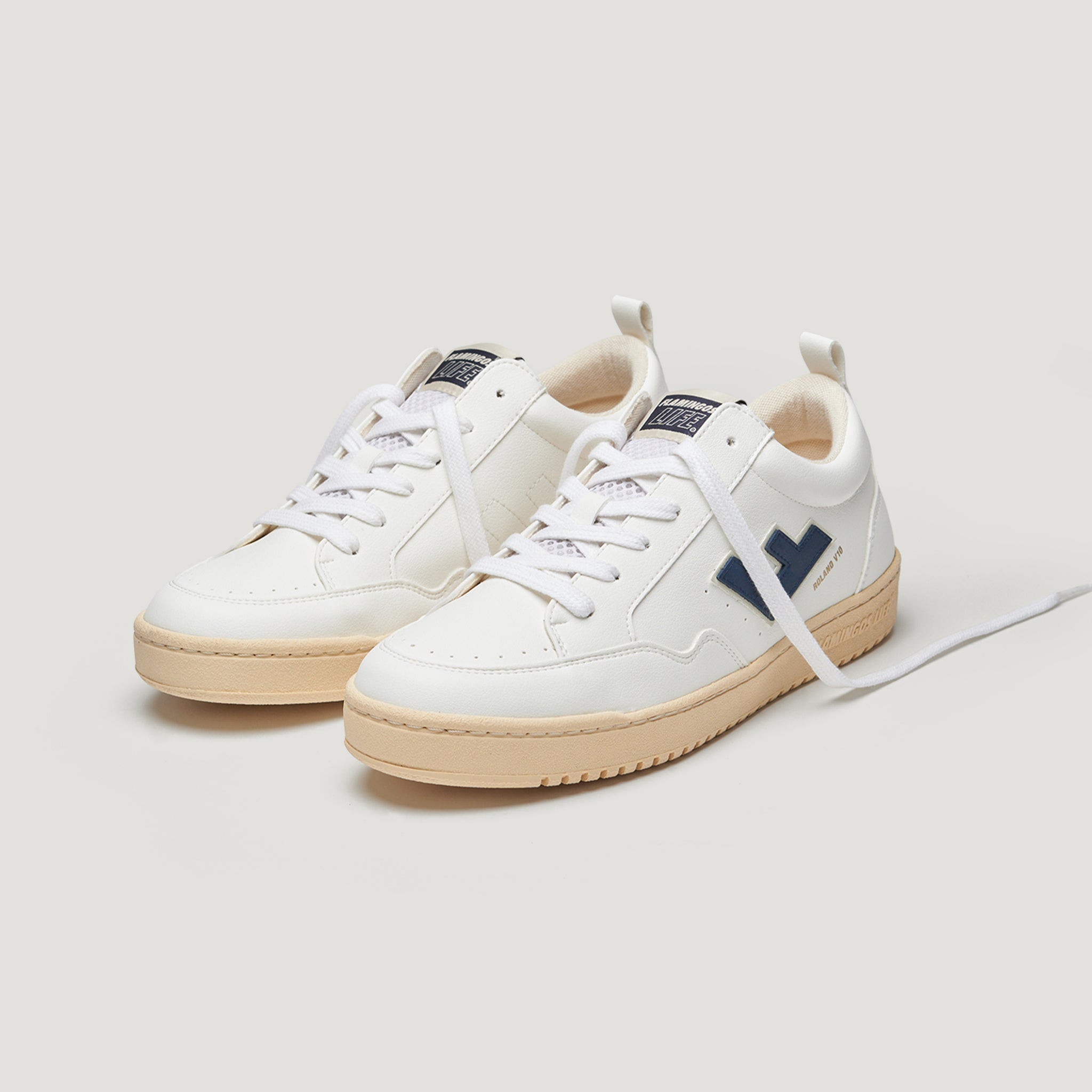 Weiße Sneaker mit blauer Applikation und beigem Gummisohlen, auf hellem Hintergrund platziert.