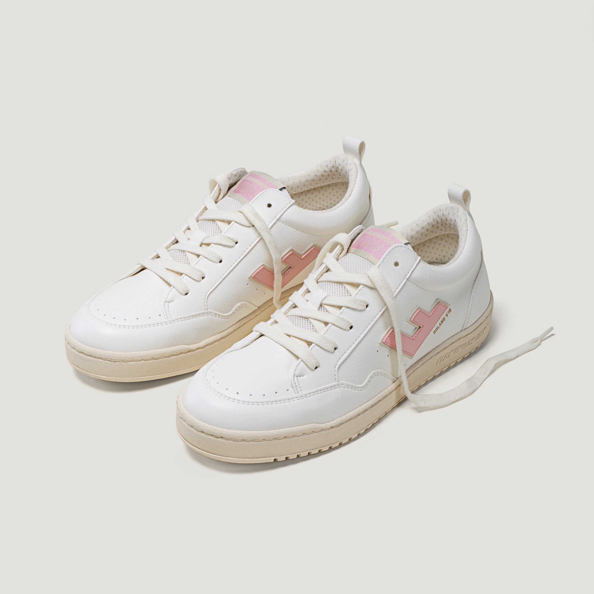 Weiße Sneakers mit rosa Details und beigem Sohlendesign auf einem hellen Hintergrund.