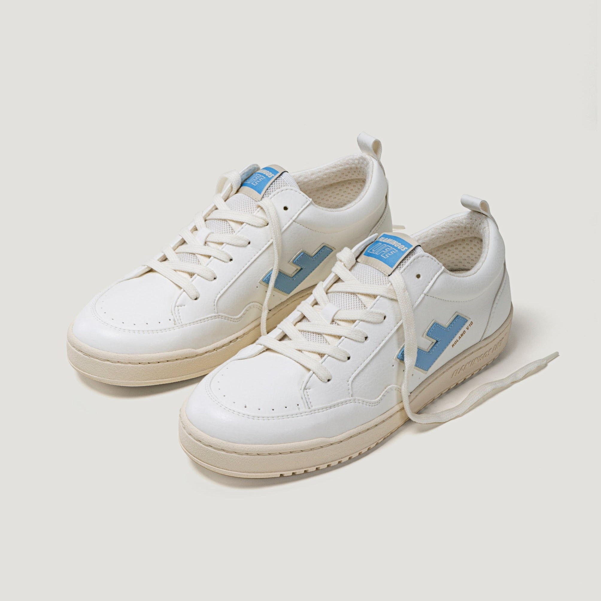 Weiße Sneaker mit hellblauen Details und cremefarbener Sohle, auf einem hellen Hintergrund.