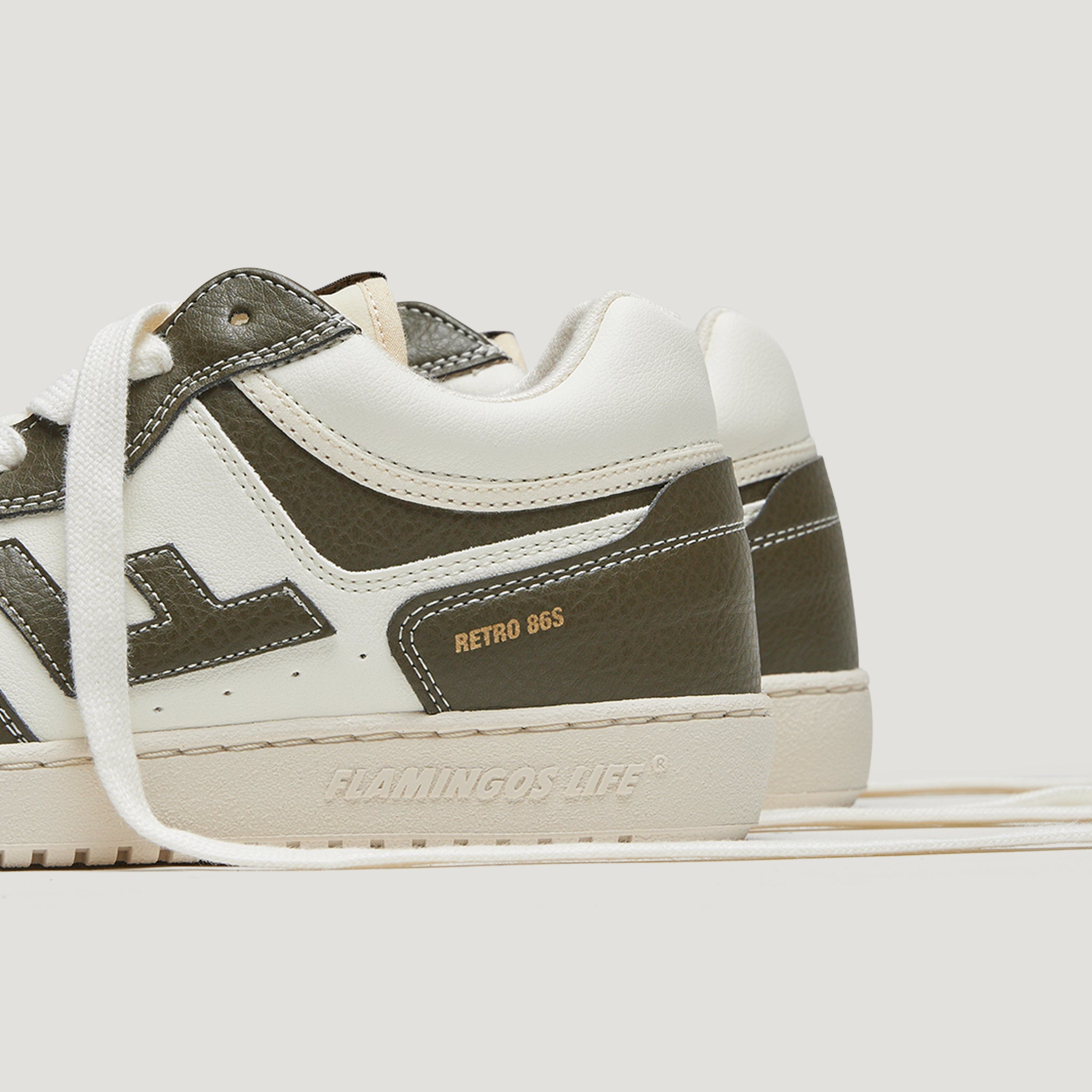 Weiße und olivgrüne Sneaker von Flamingos Life im Retro 86S-Design auf hellem Hintergrund.