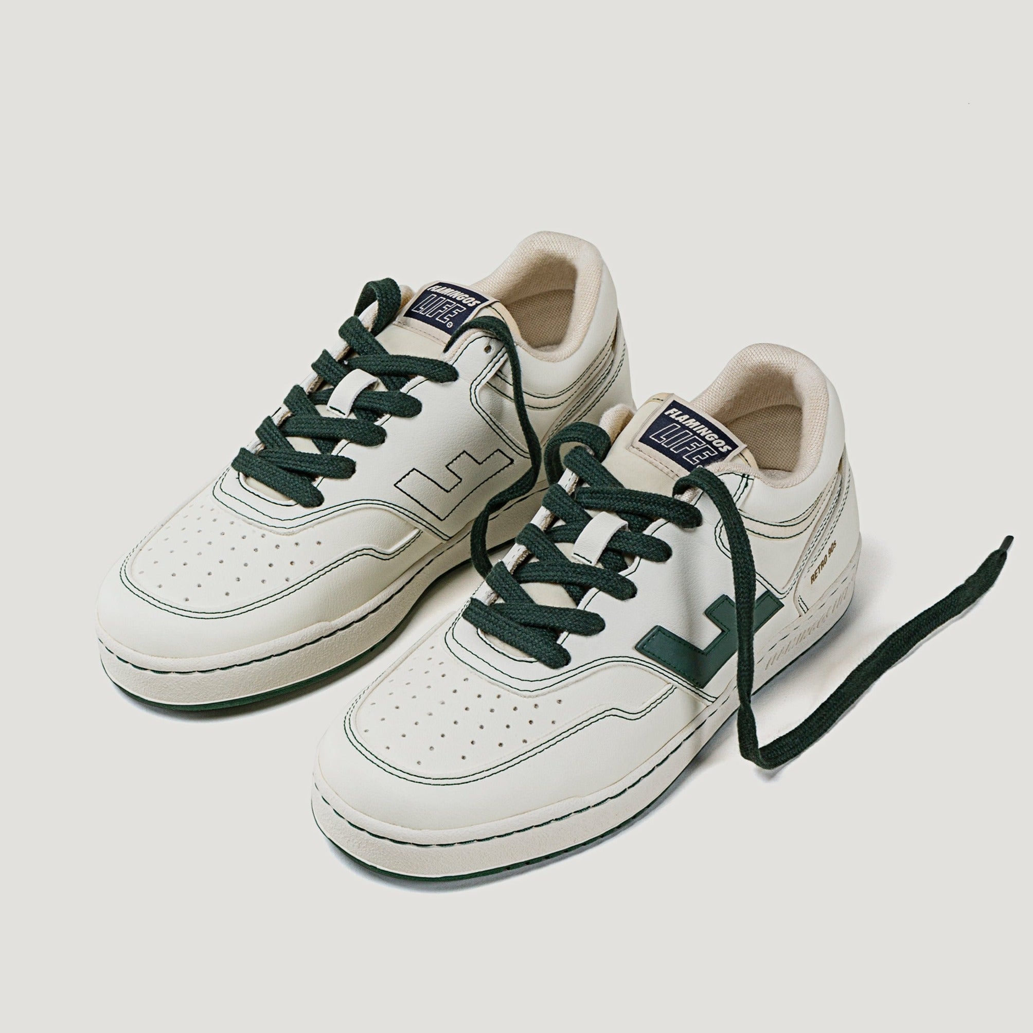 Weiße Sneaker mit grünen Akzenten und schwarzen Schnürsenkeln auf hellem Hintergrund.