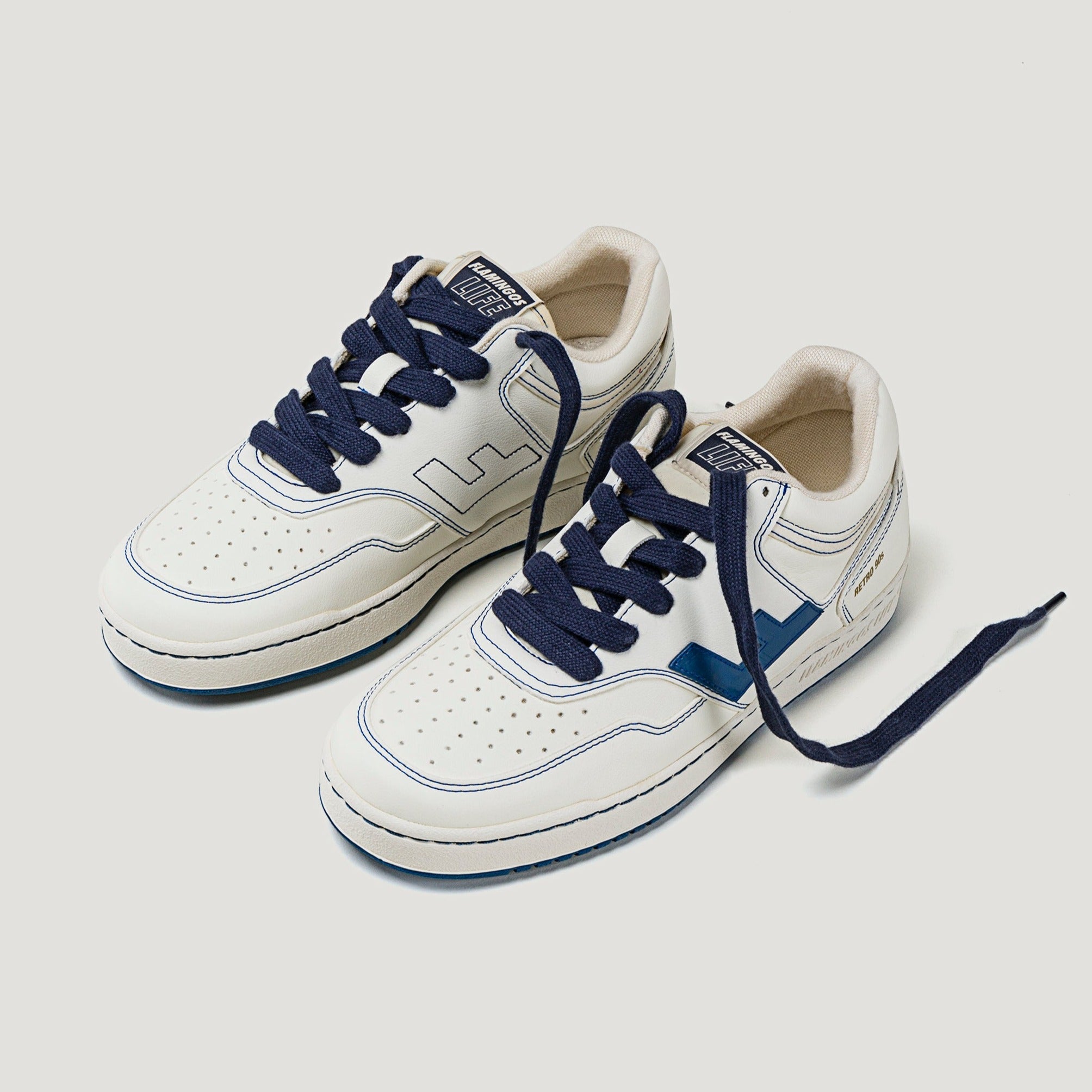 Weiße Turnschuhe mit dunkelblauen Schnürsenkeln und blauen Akzenten, auf neutralem Hintergrund liegend.