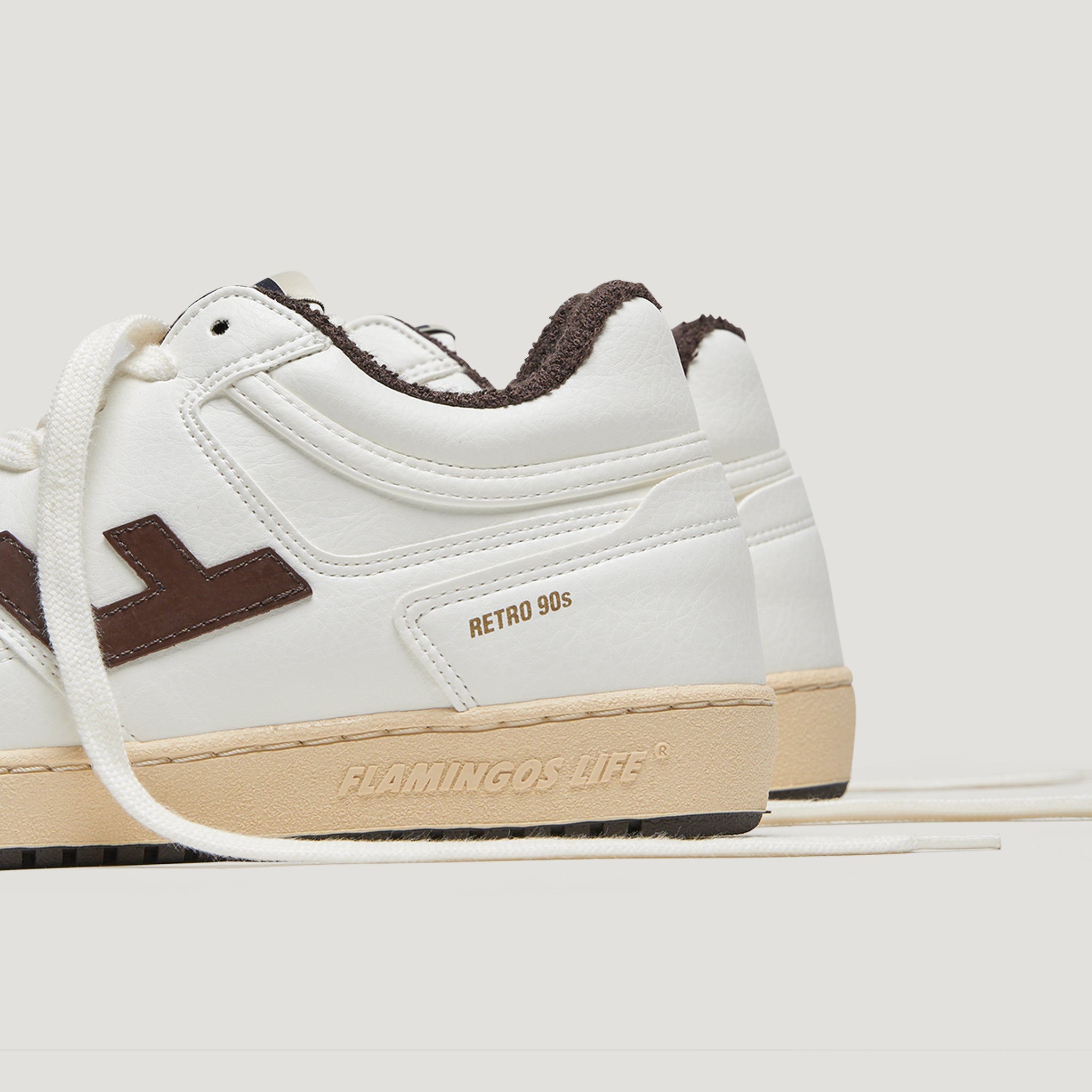Weißer Sneaker mit dunkelbraunen Details und der Aufschrift "Retro 90s" sowie "Flamingos Life" auf der Sohle.