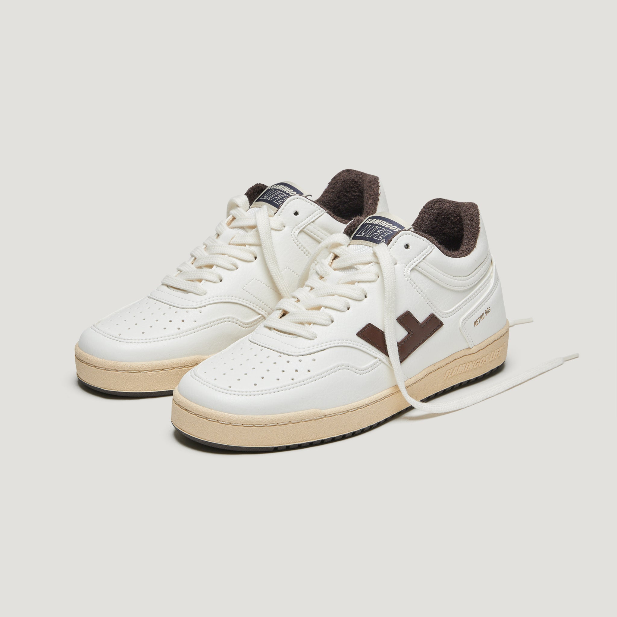 Weiße Turnschuhe mit braunen Akzenten und beiger Sohle auf einem hellen Hintergrund.