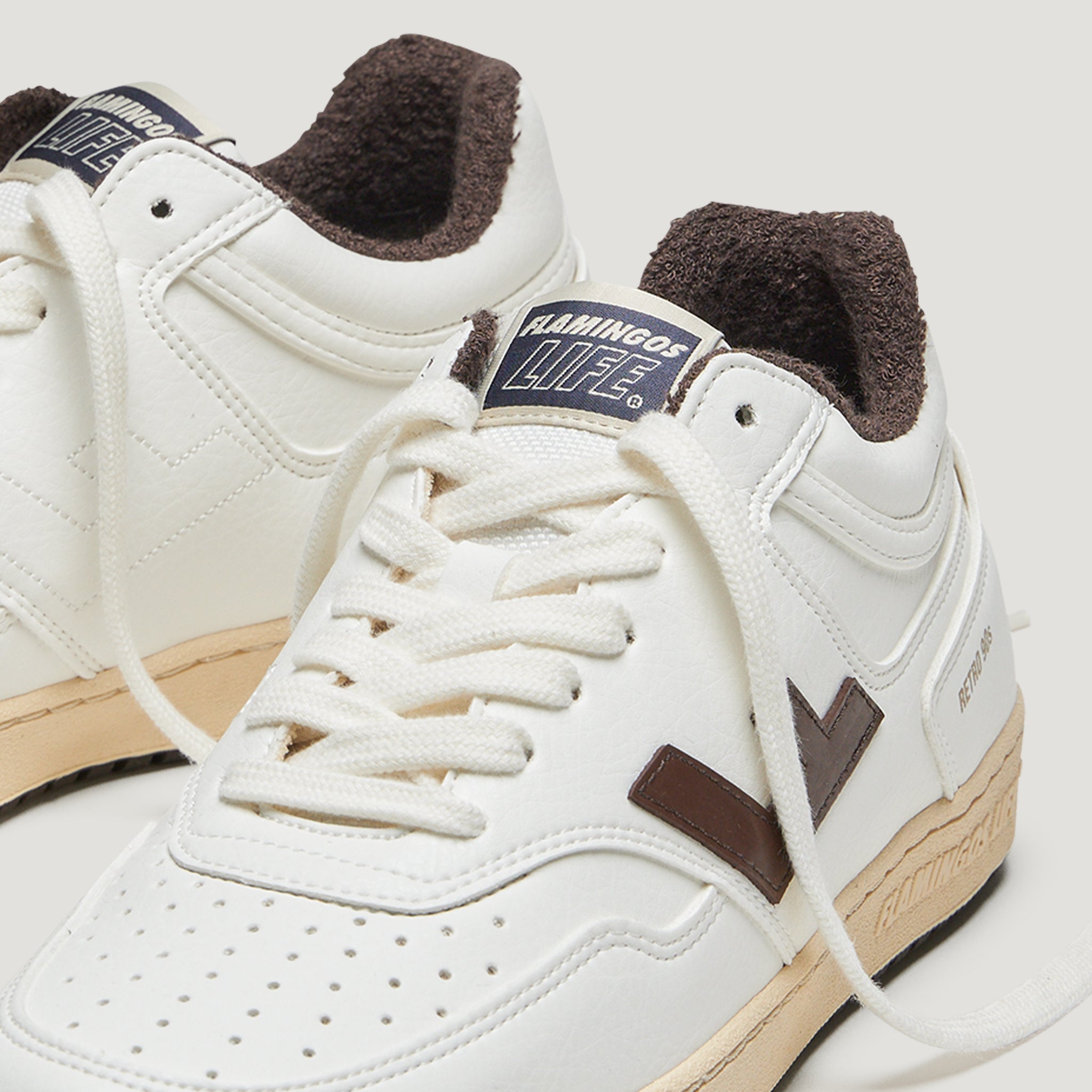 Weiße Sneaker mit braunen Details und dem Logo "Flamingos Life" auf der Zunge, gezeigt in Nahaufnahme.