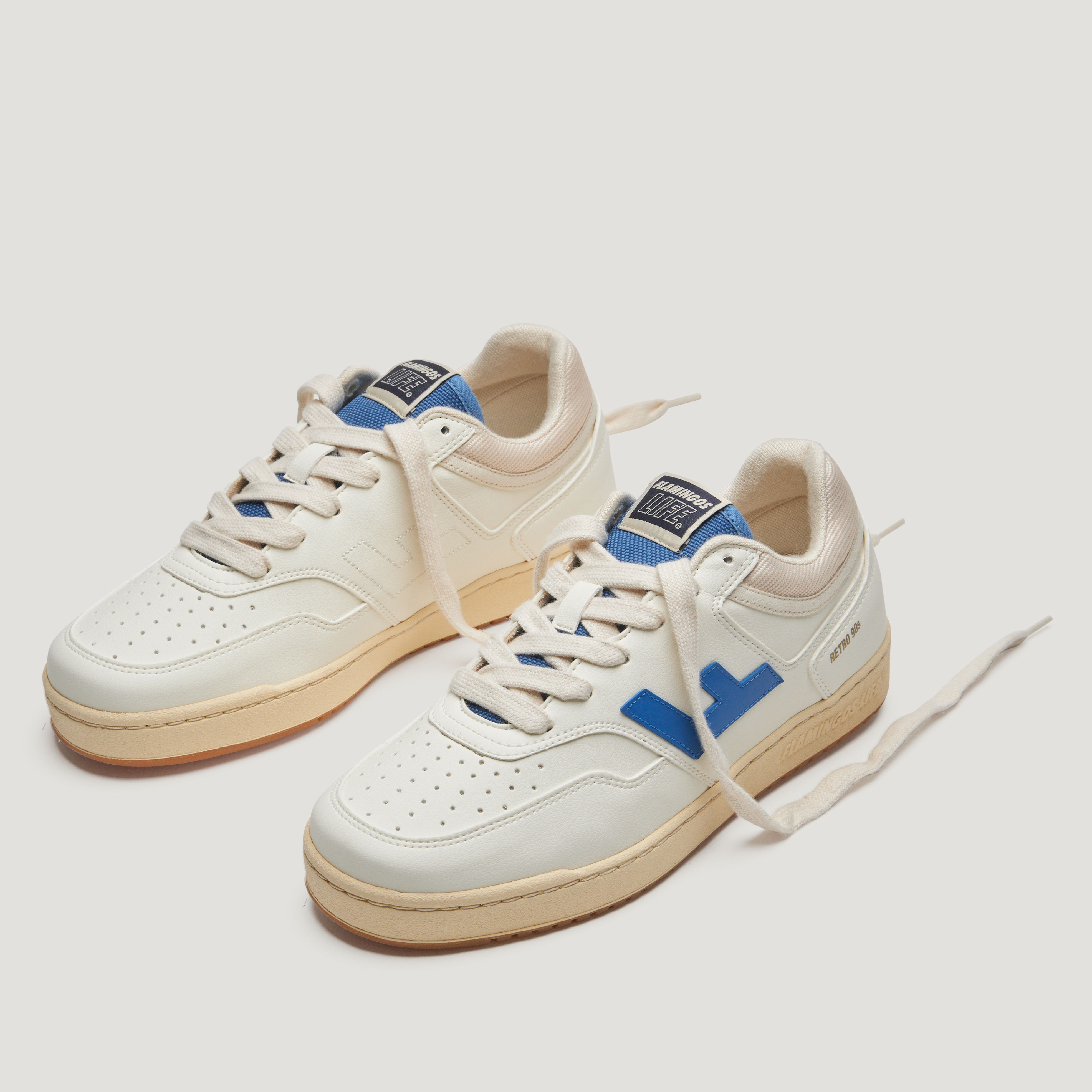 Weiße Sneaker mit blauen Details und beige Sohle, auf weißem Hintergrund fotografiert.