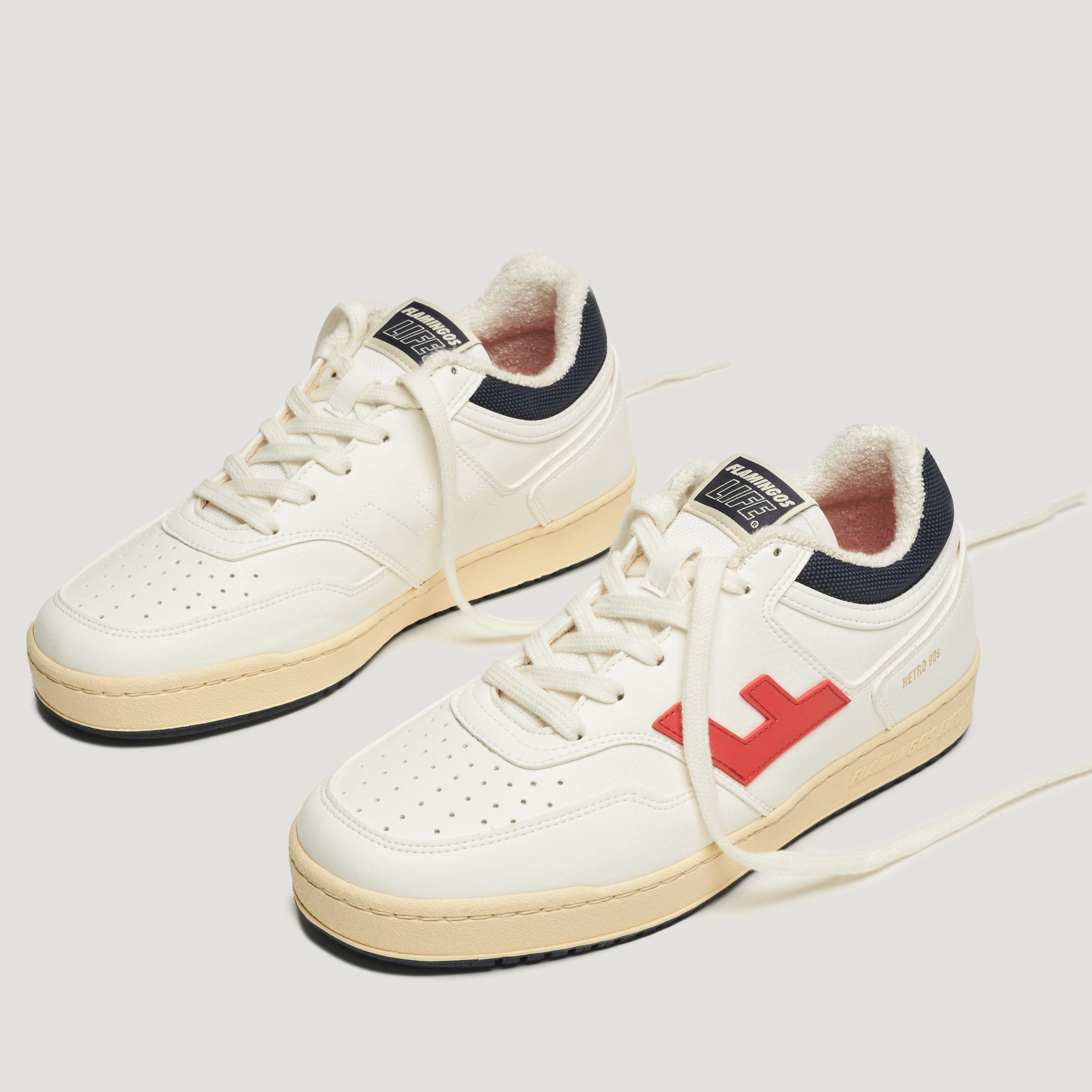 Weiße Turnschuhe mit rotem Logo an der Seite, schwarzem Futter und Vintage-Sohle auf weißem Hintergrund.